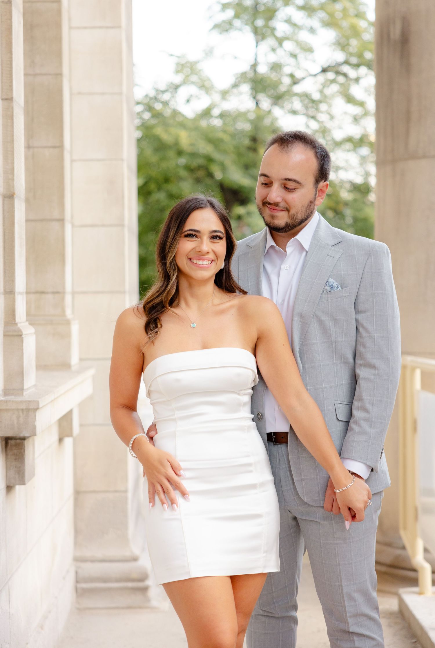 Happy couple in formal wear pose together among grand stone columns.