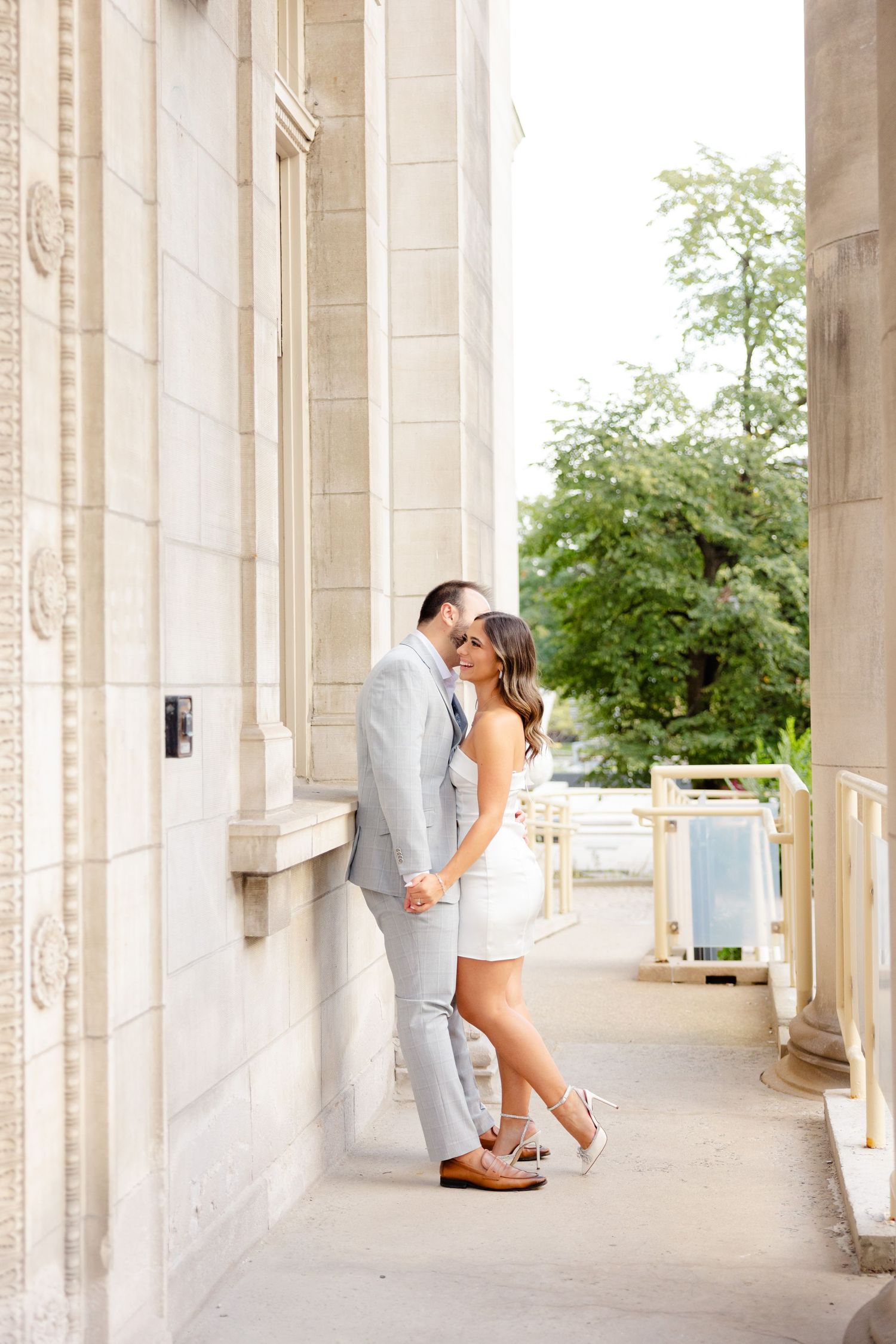 A couple in coordinated white and gray outfits share a romantic moment on a covered terrace.
