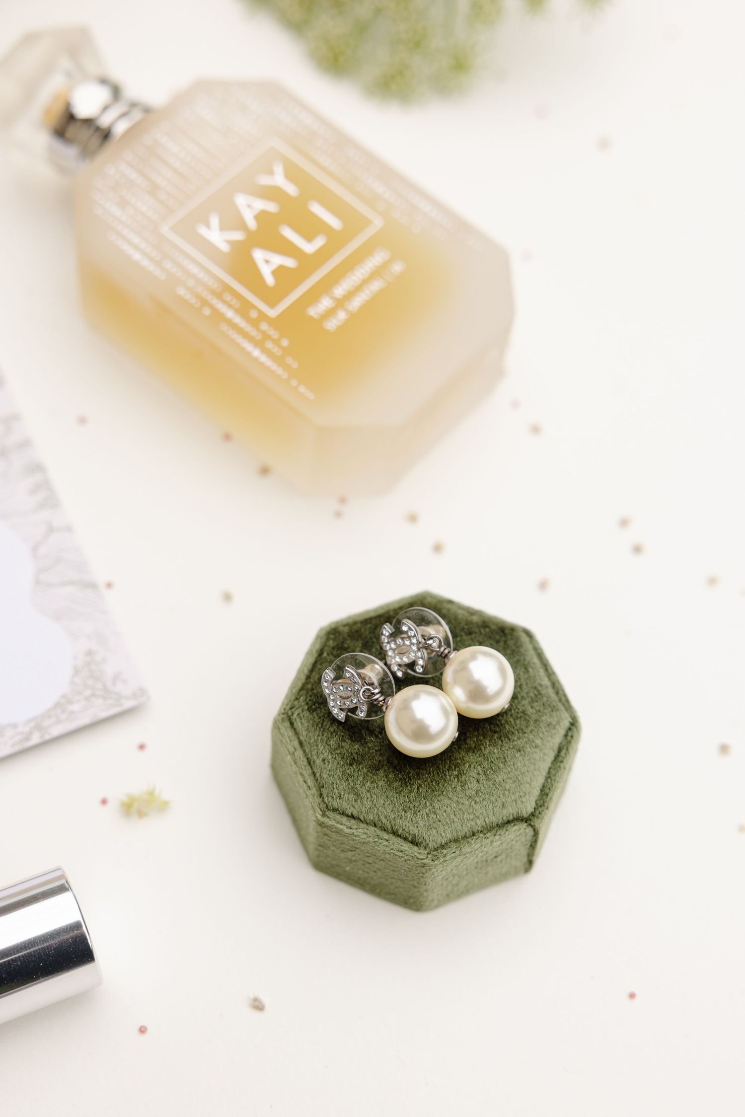 Elegant pearl and crystal jewelry arranged on sage green hexagonal displays with perfume bottles in background.