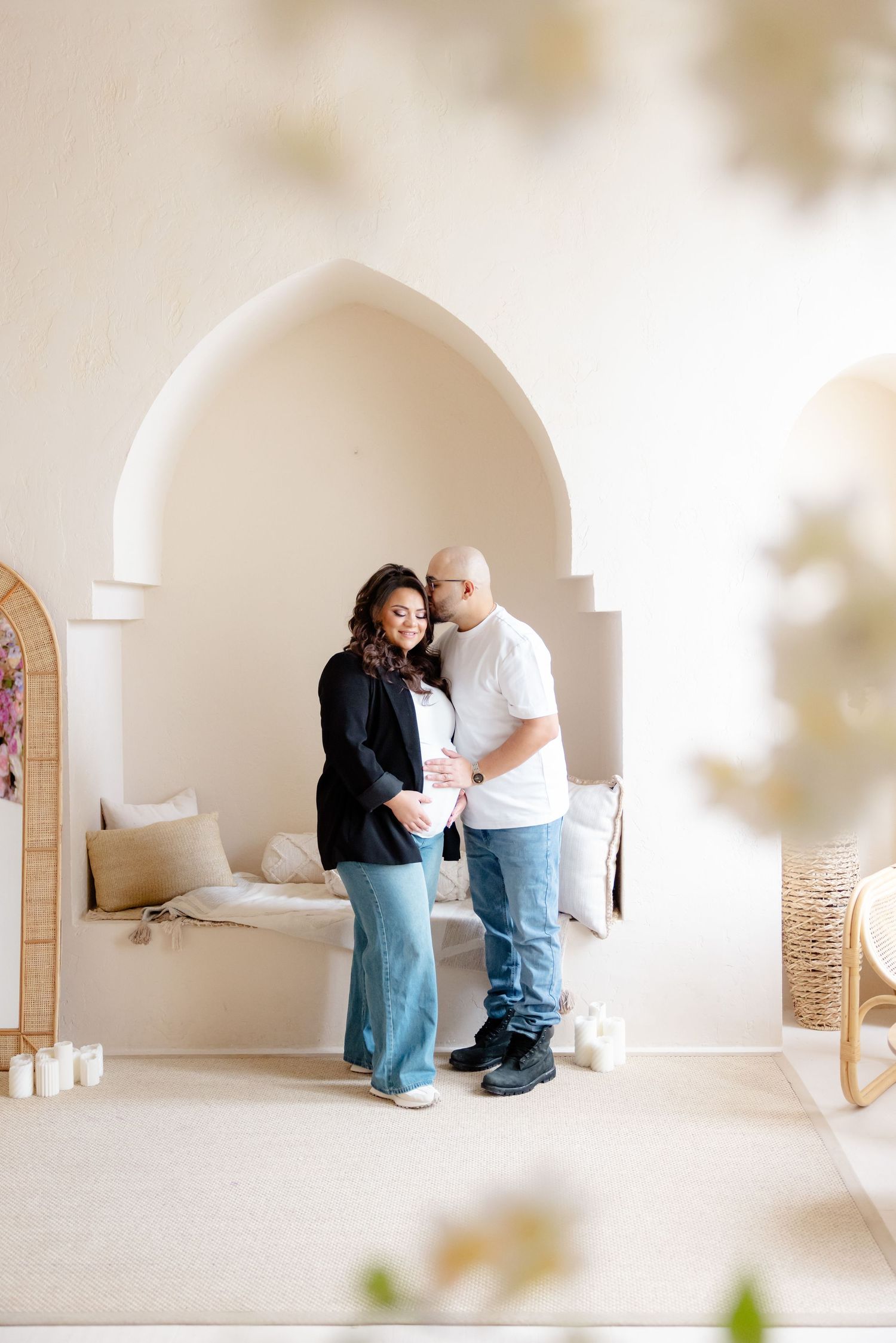 A couple shares an intimate moment in a serene white arched alcove decorated with candles and boho elements.