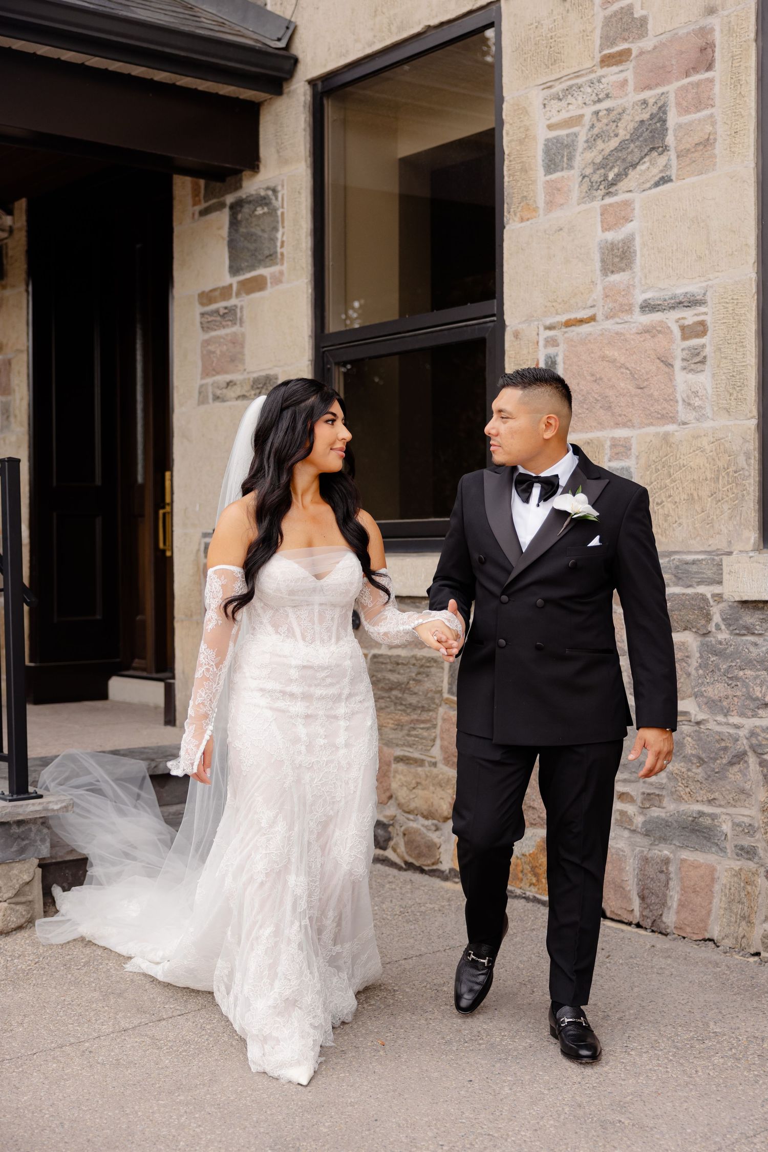 A newlywed couple walks together along a stone building exterior in three sequential romantic wedding photos.