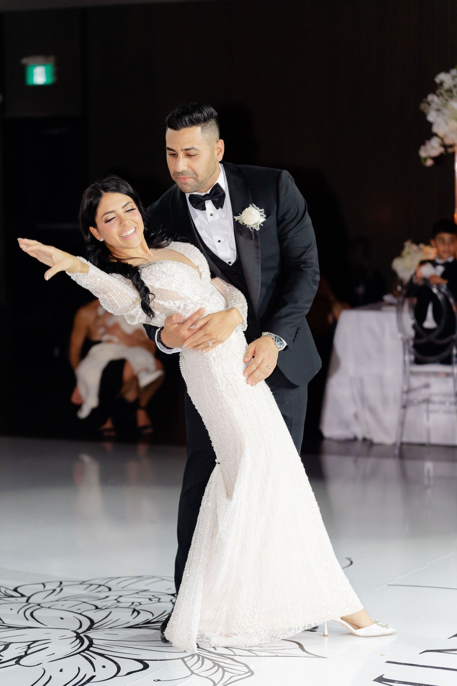 Couple performs romantic dip during wedding dance on decorated ballroom floor.