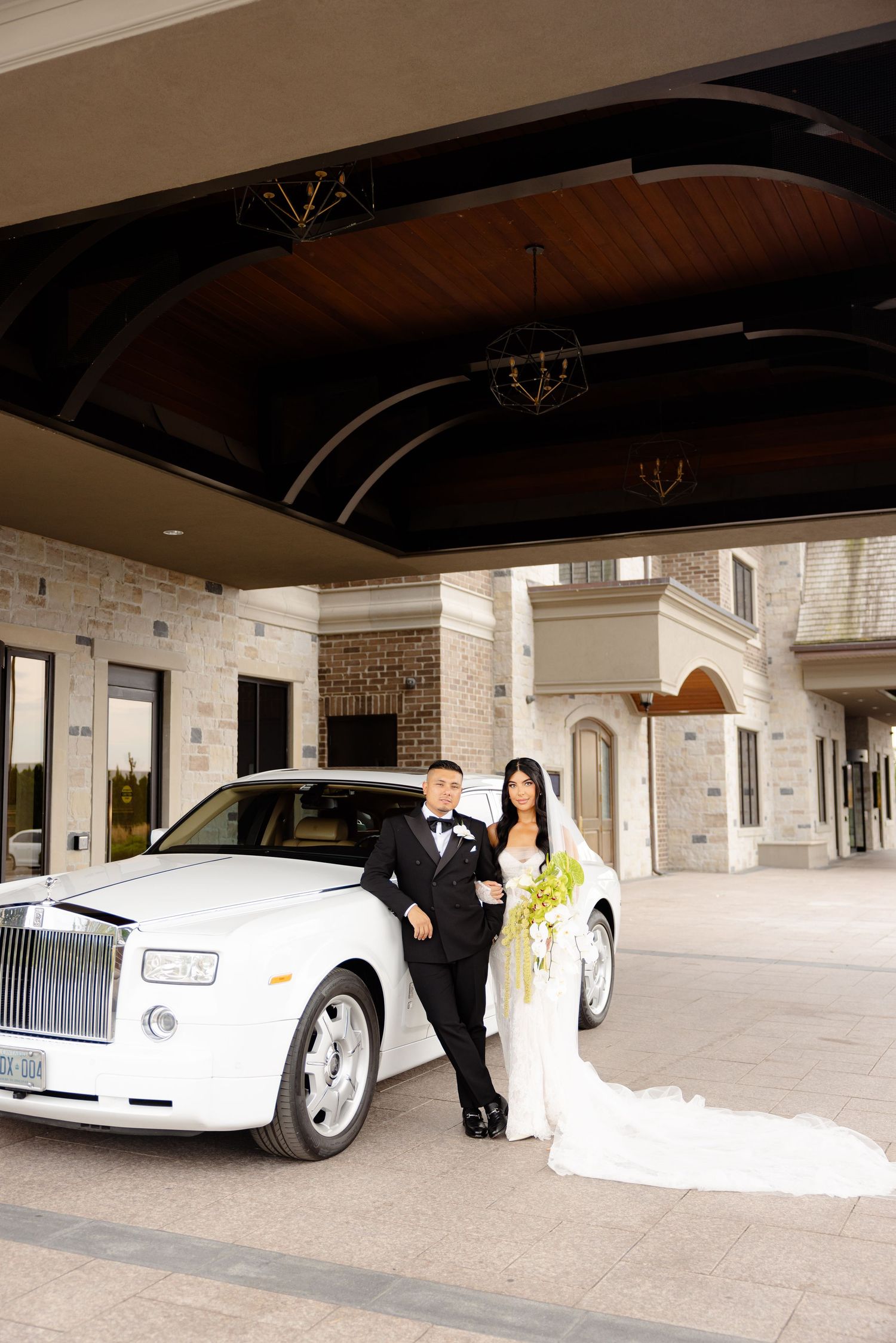Elegant wedding scene with luxury white Rolls Royce and brick facade building entrance.