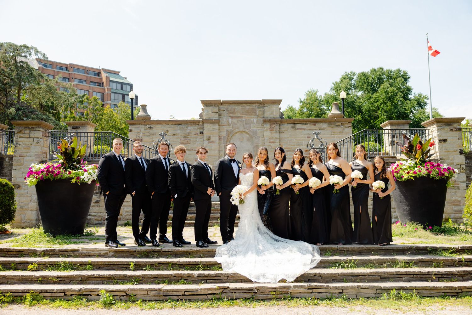Wedding party poses on stone steps and walkway with bridesmaids in black dresses and groomsmen in black suits.