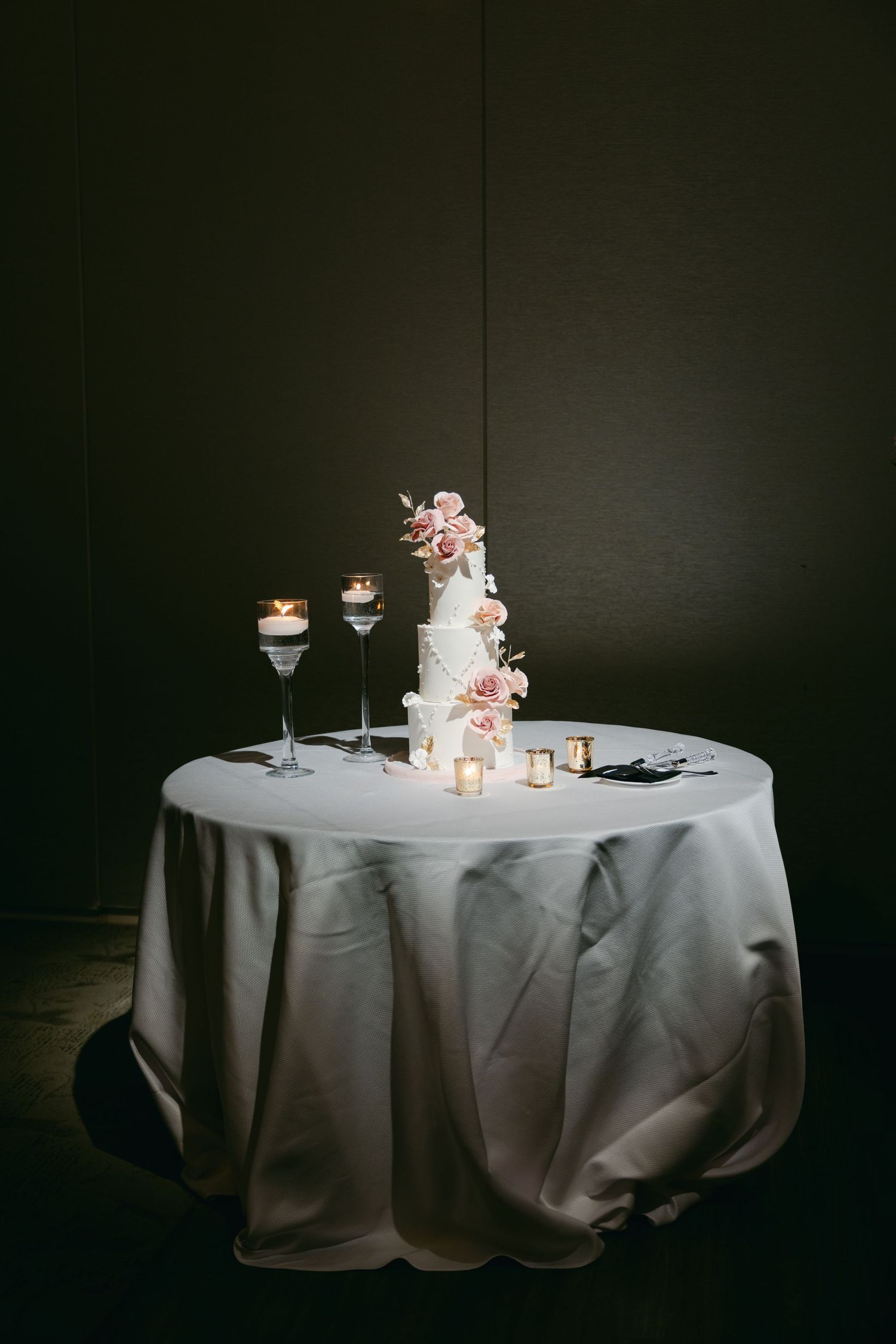 Elegant wedding cake displayed on round table with champagne glasses in dramatic lighting.