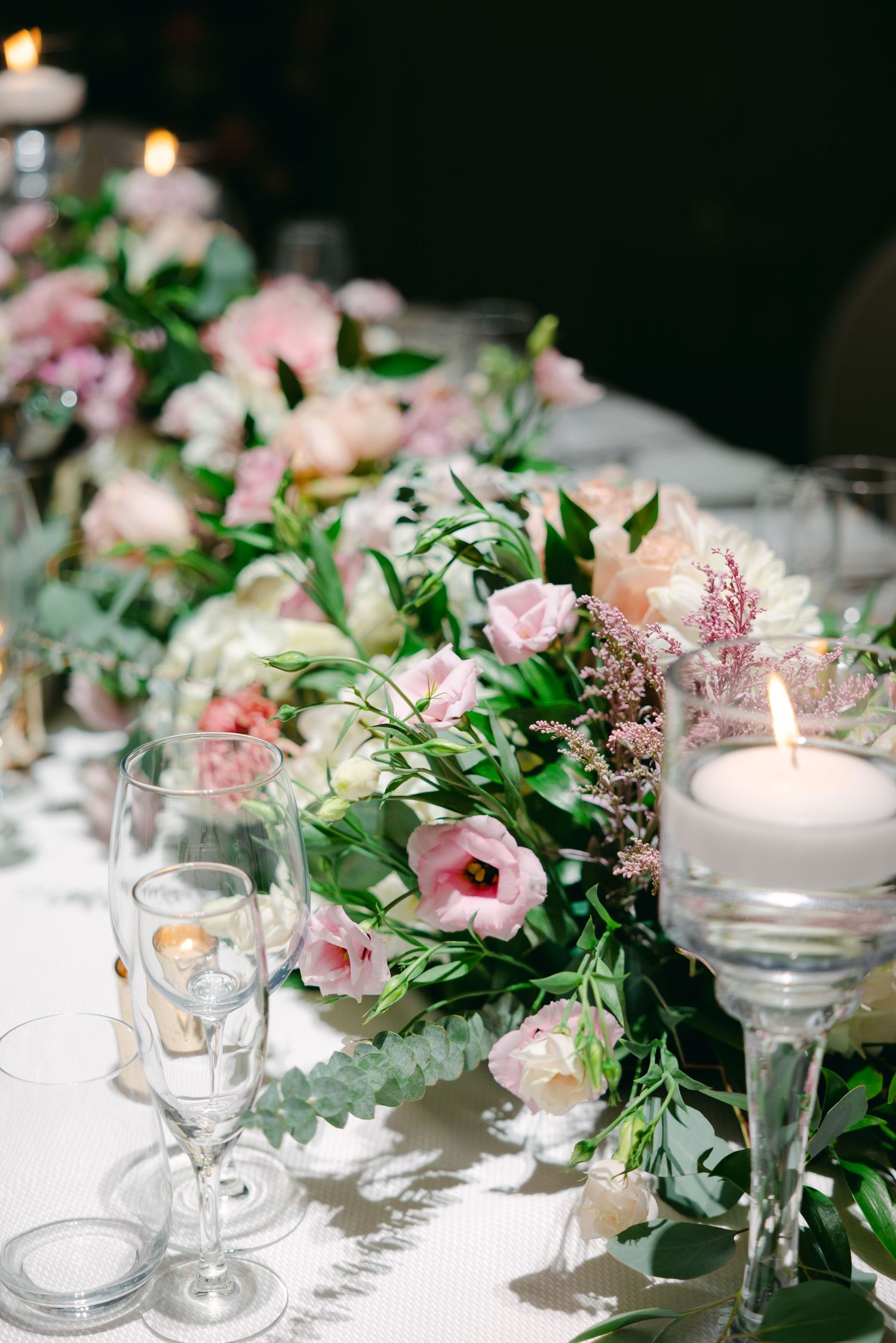 Close-up of wedding table garland with pink flowers, greenery and floating candles.