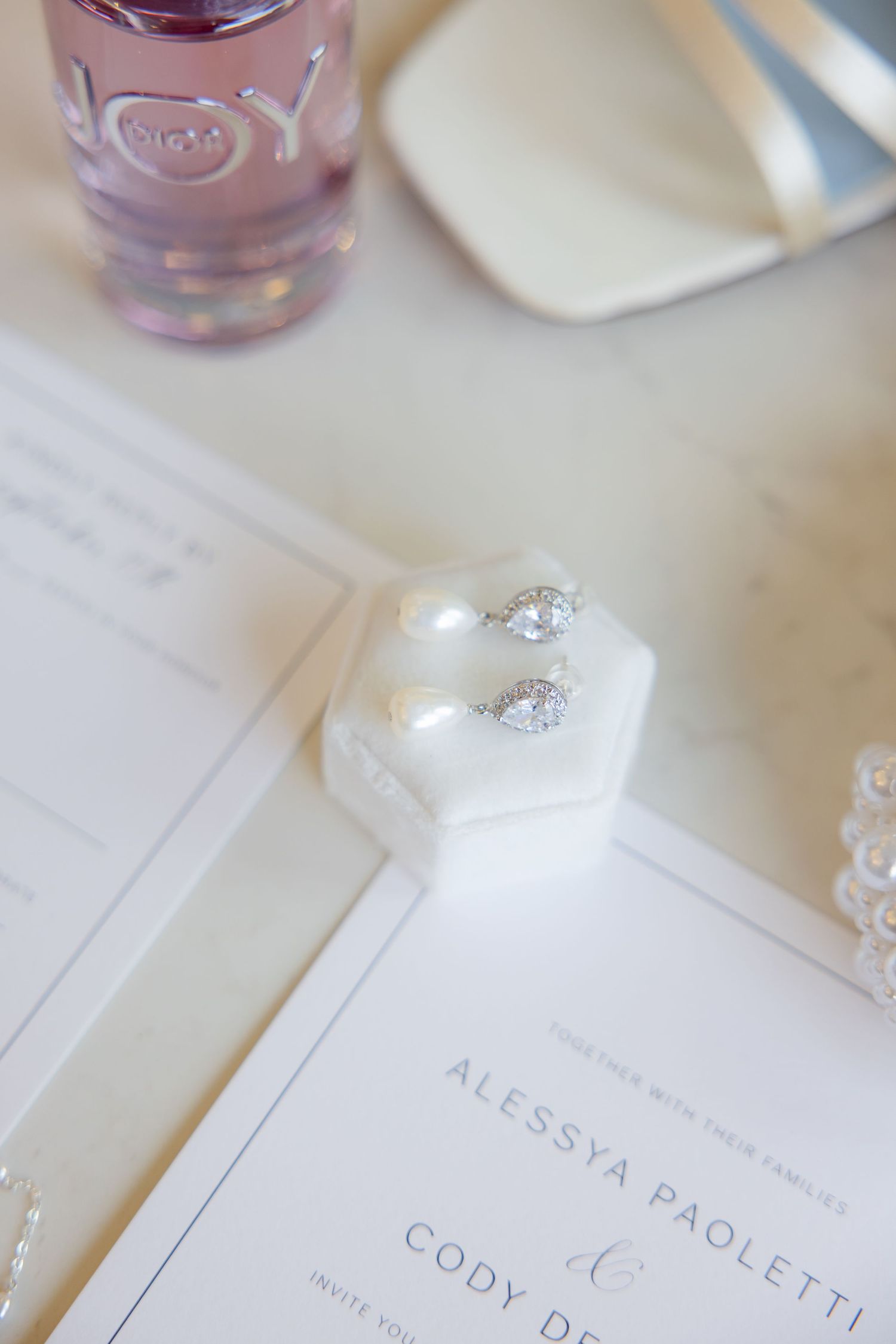 Wedding invitation and diamond earrings with pink perfume bottle.