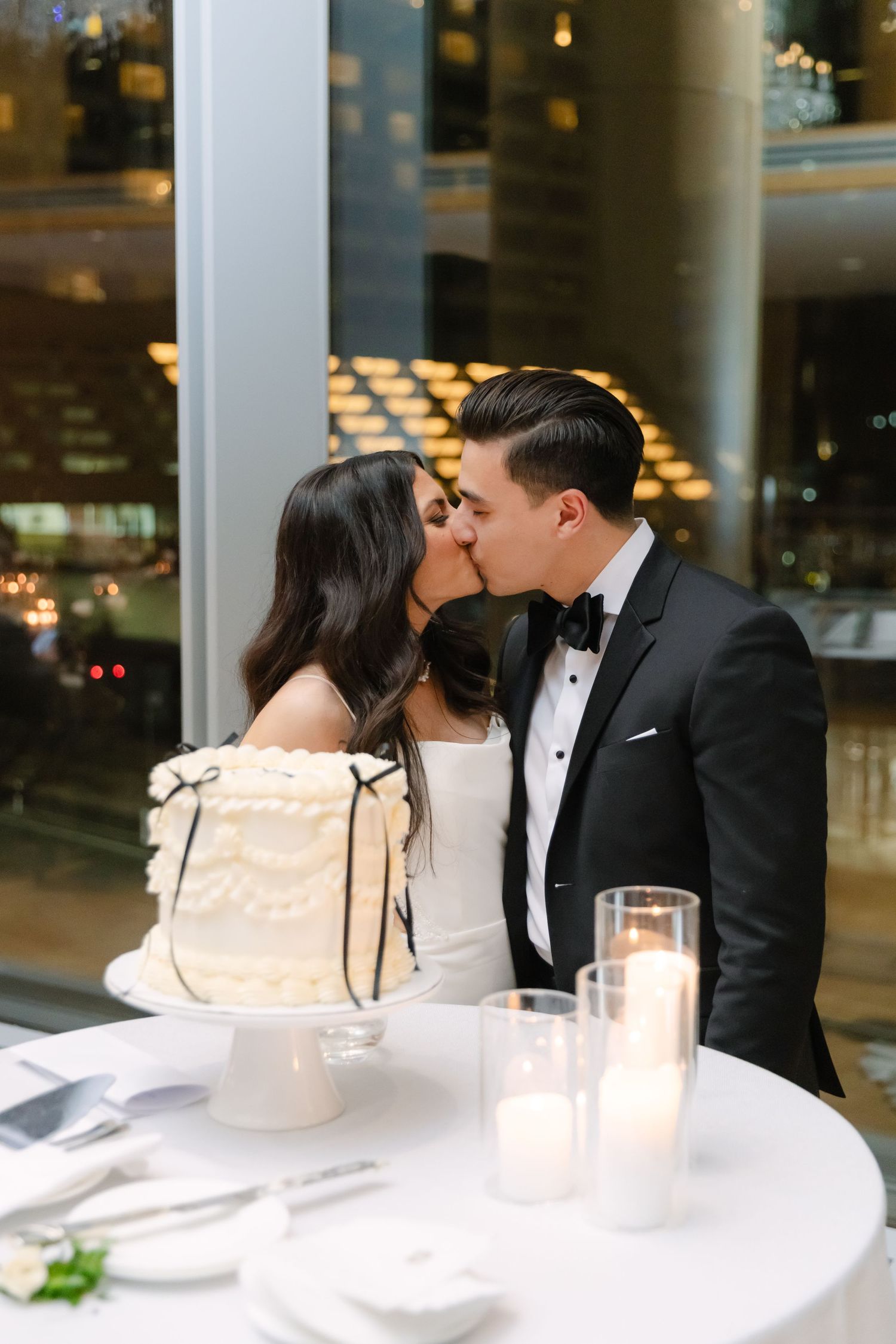 A couple shares a romantic moment by their elegant white wedding cake.
