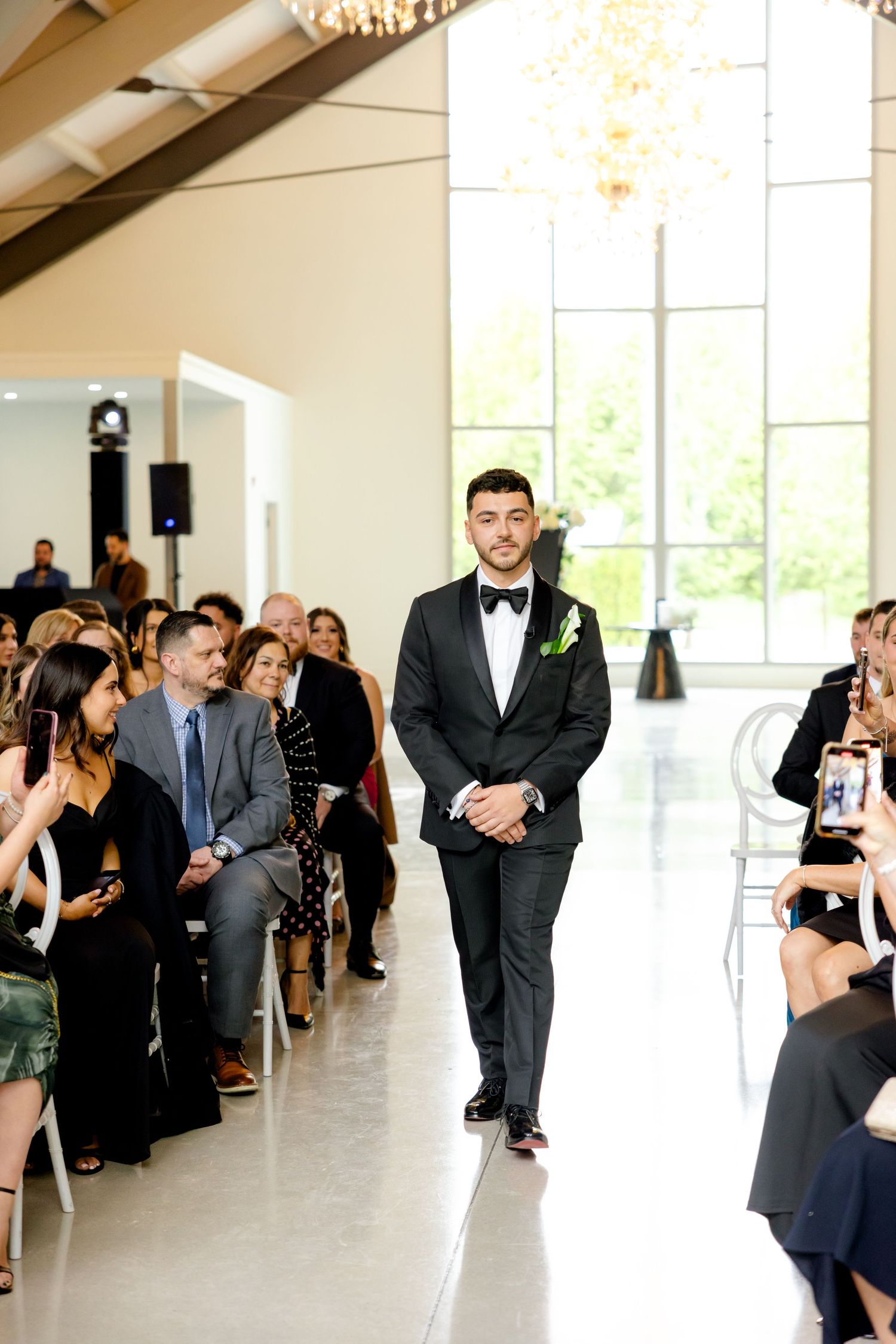 Wedding ceremony aisle with guests seated in modern white chairs in bright venue.