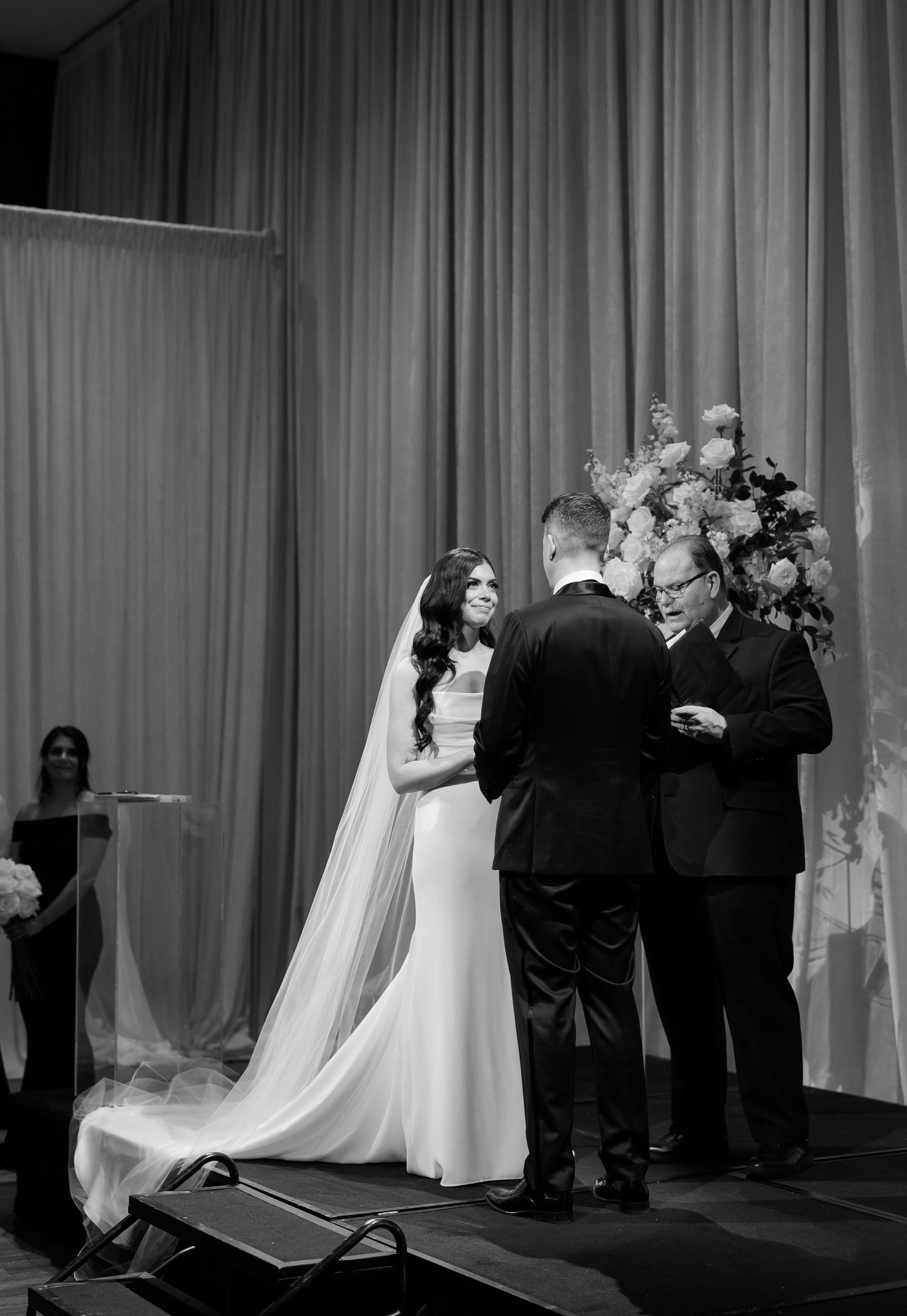 Black and white ceremony photo showing elegant wedding service on elevated stage.