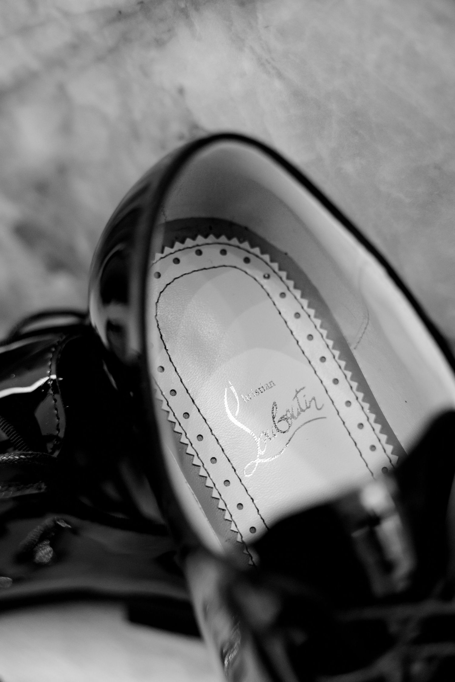 Close-up black and white detail of a luxury shoe insole showing decorative brogue perforations.