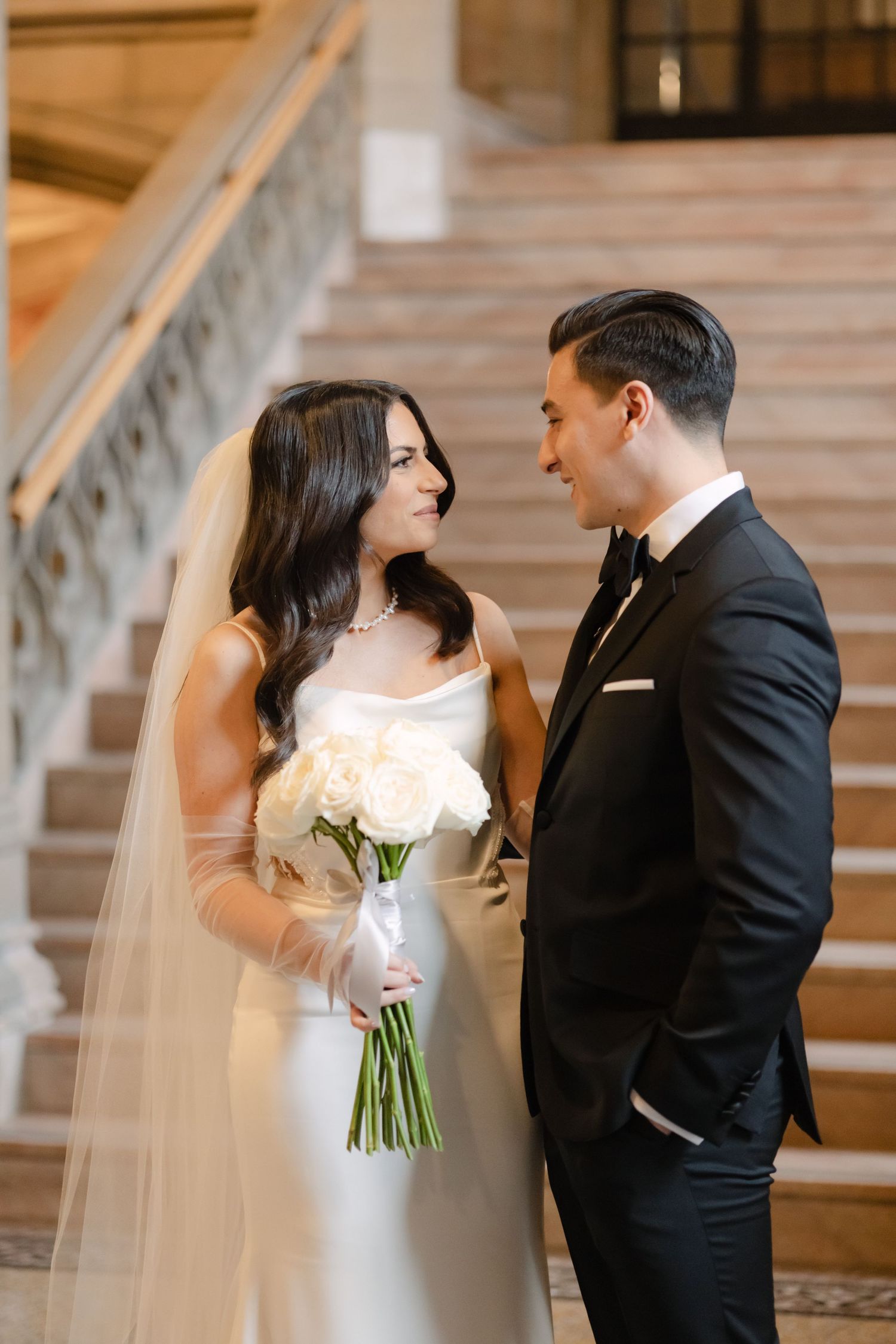 A couple in wedding attire shares an intimate moment on an elegant staircase.