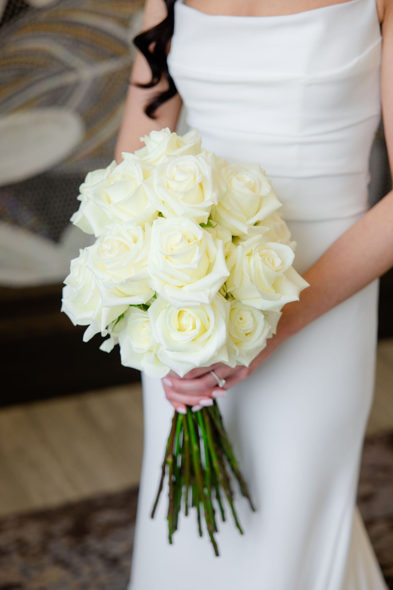 Close-up of a classic white rose wedding bouquet held against a white wedding dress.