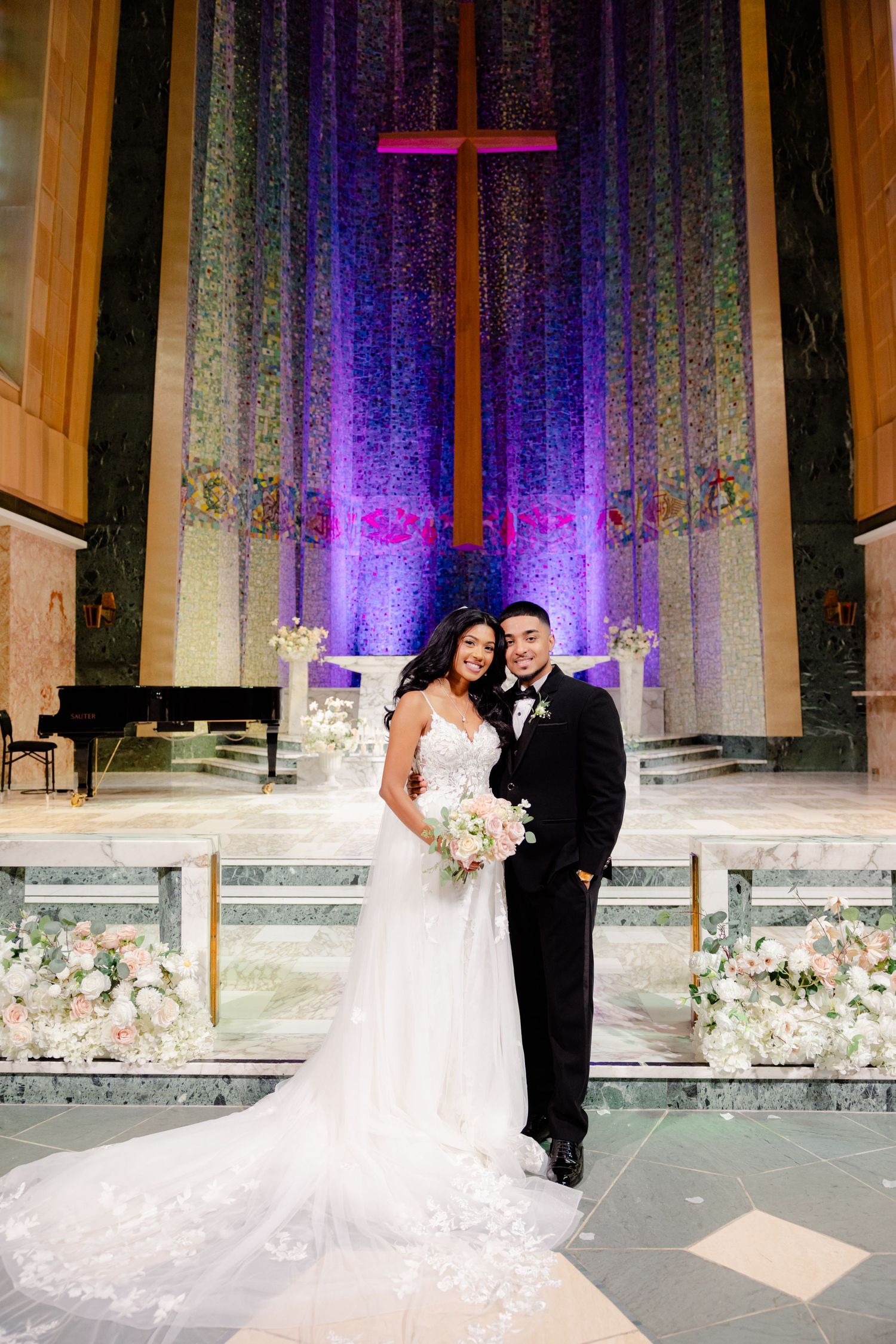 Elegant wedding portrait in church with dramatic purple backlighting and floral arrangements.