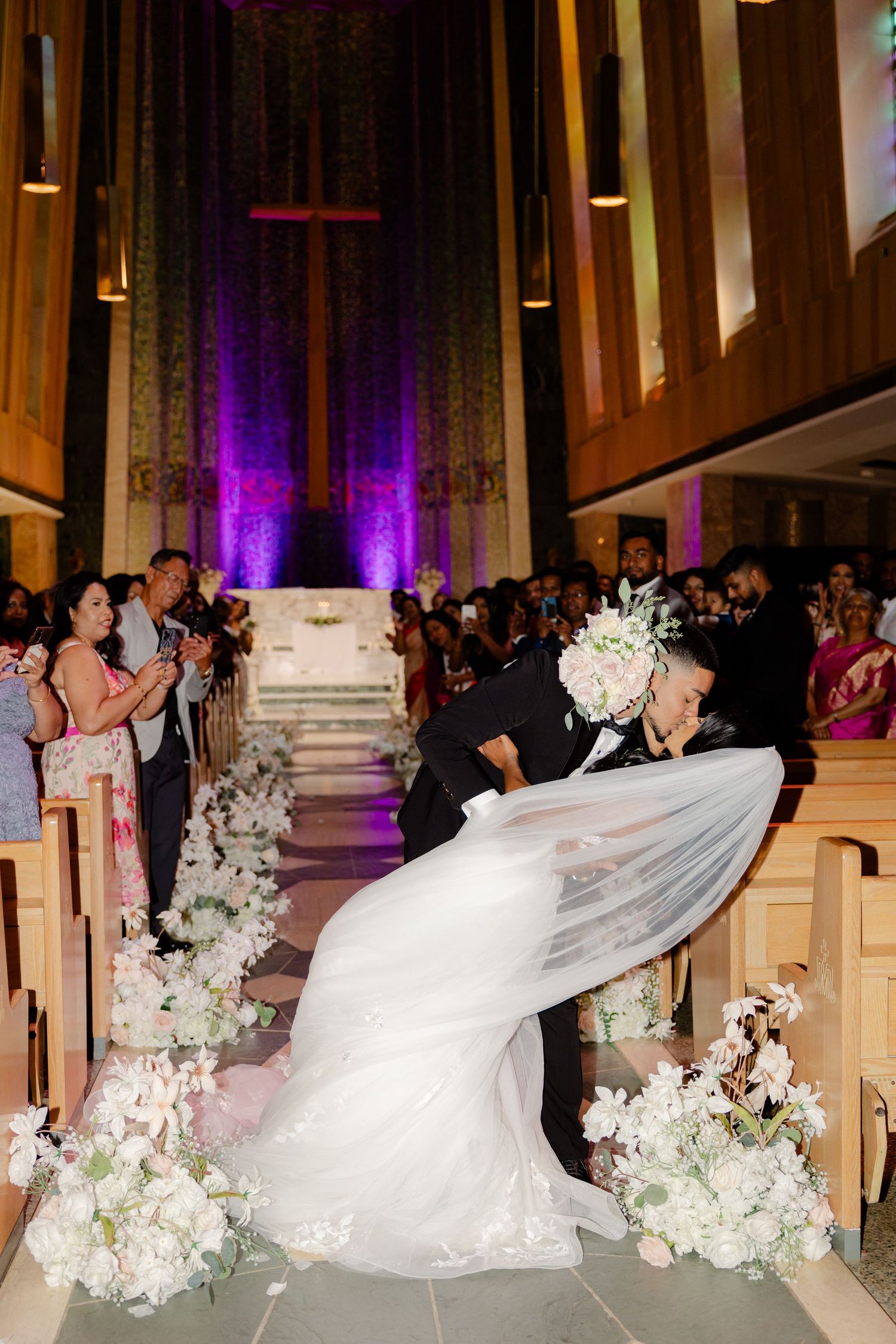 A dramatic wedding kiss captured in a church with purple lighting and floral decorations.