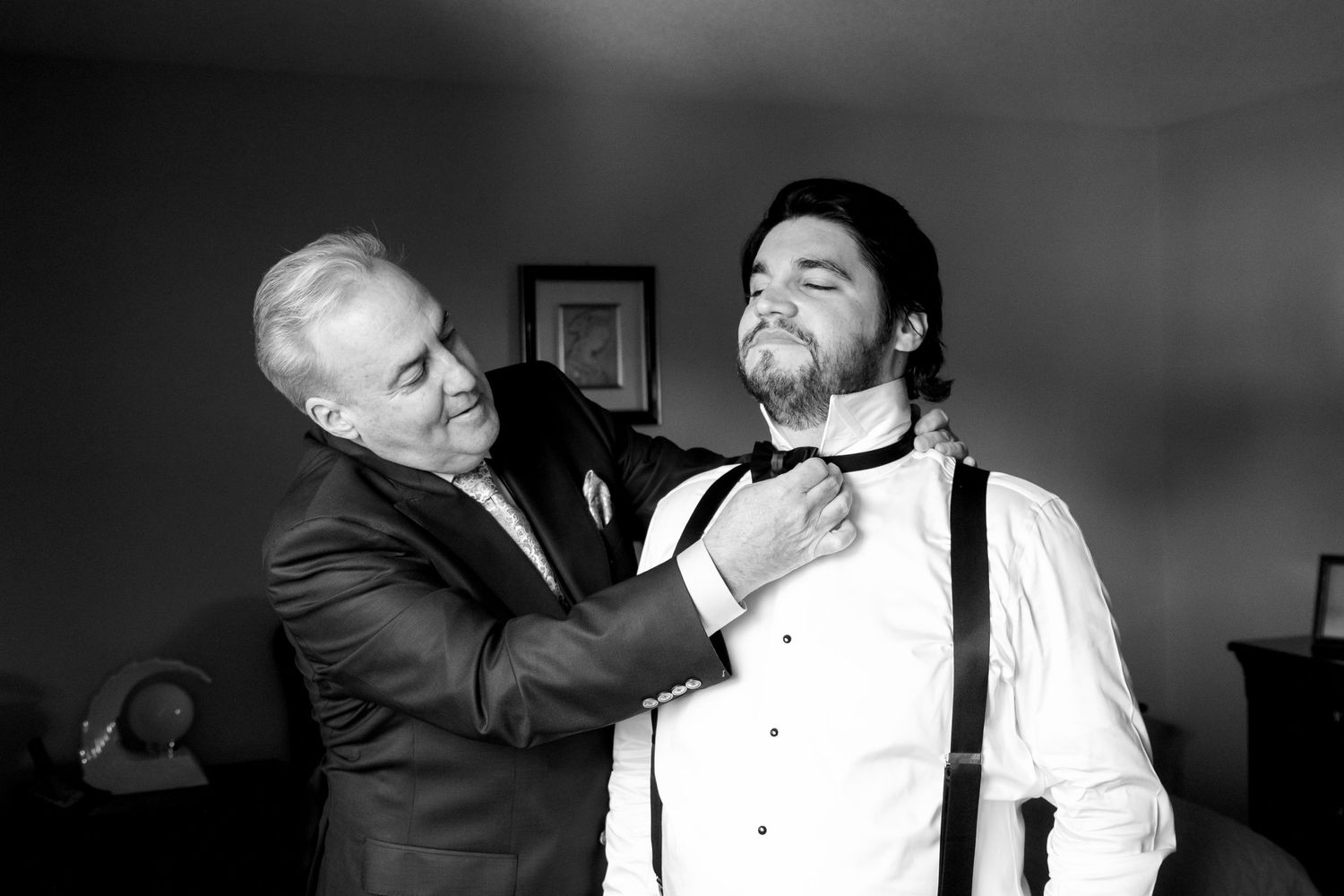 Black and white photo of formal bow tie adjustment in wedding preparation.