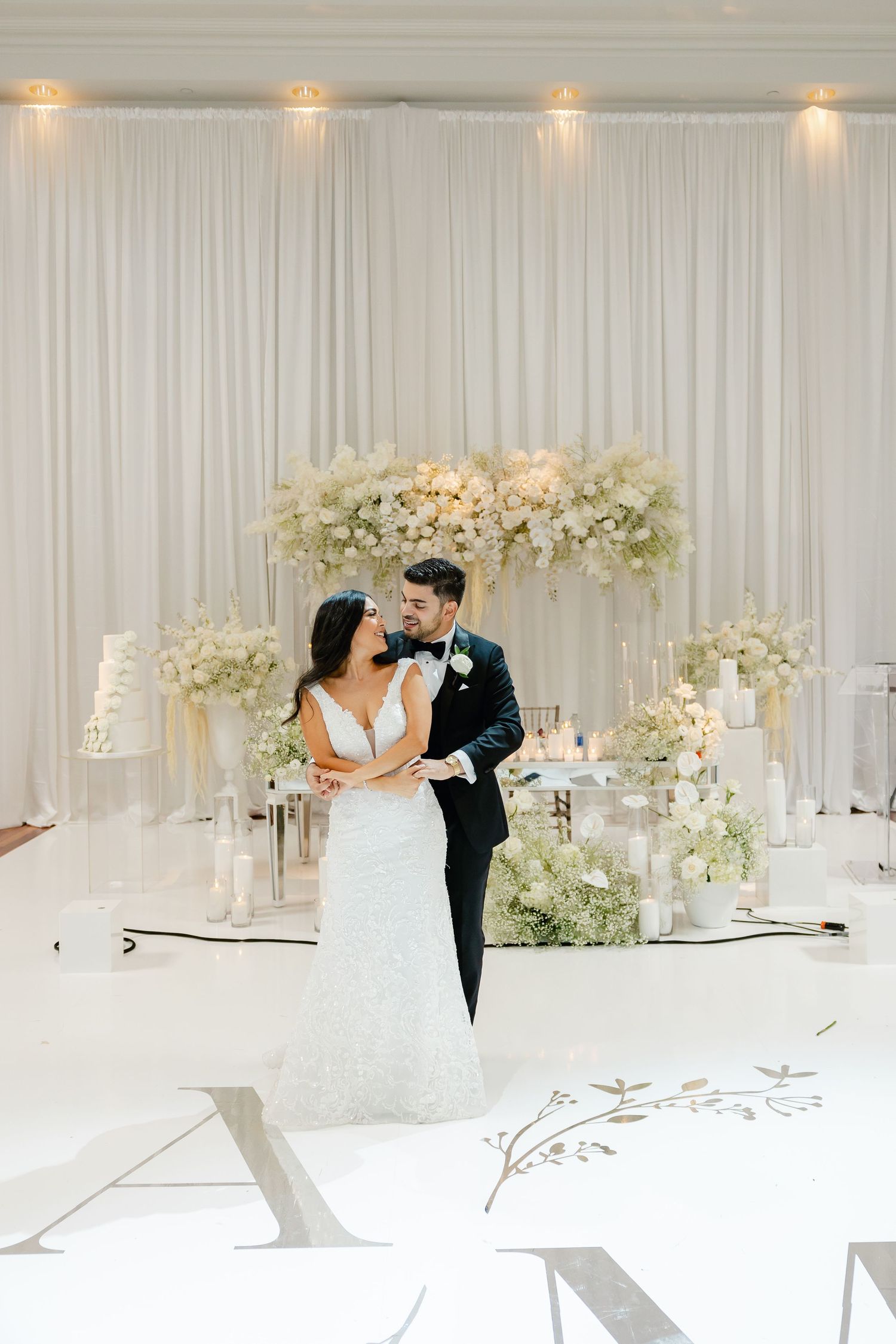 Newlyweds share an intimate moment on their wedding day surrounded by white floral arrangements.