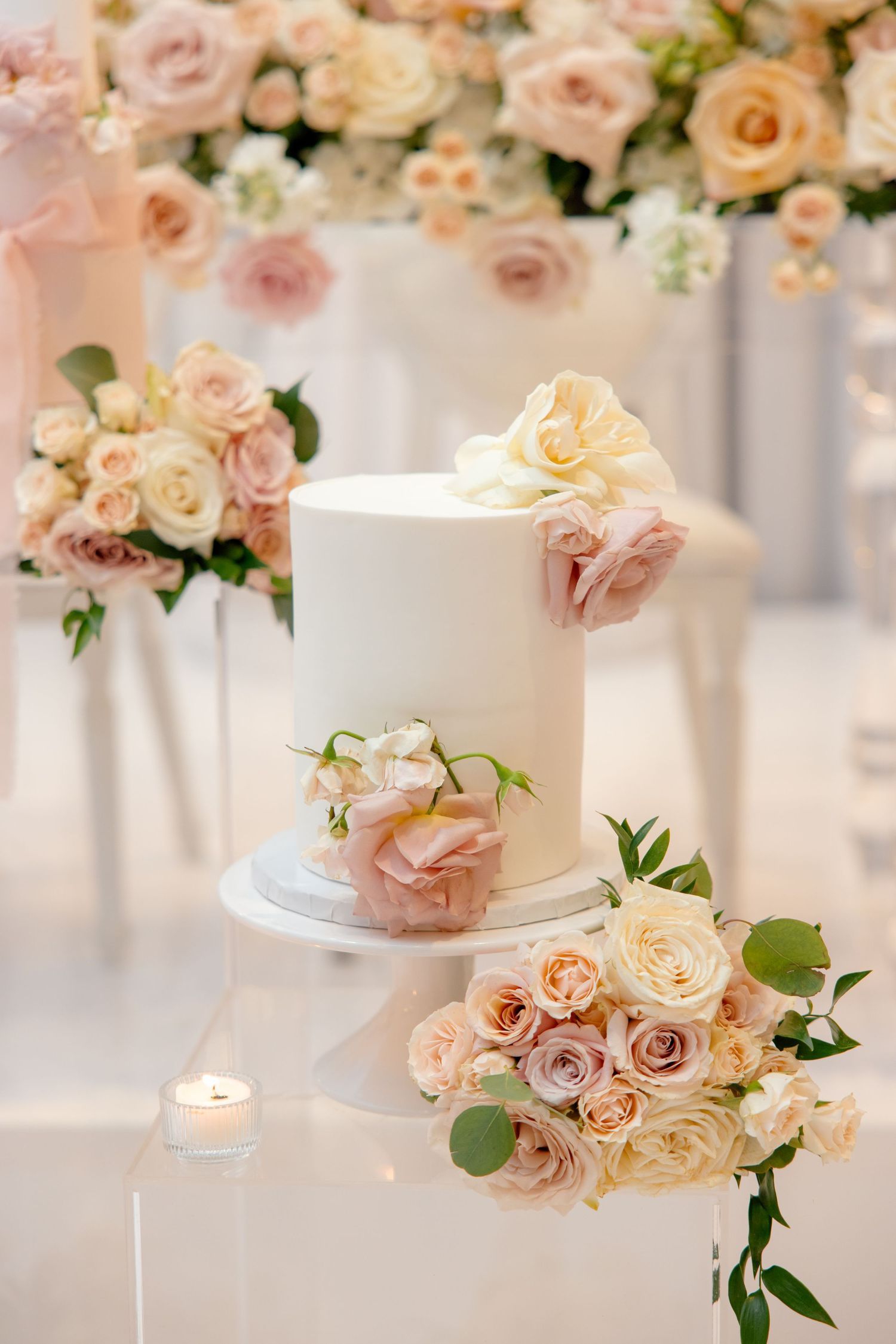 Classic white wedding cake decorated with soft pink and cream roses on a white display stand.