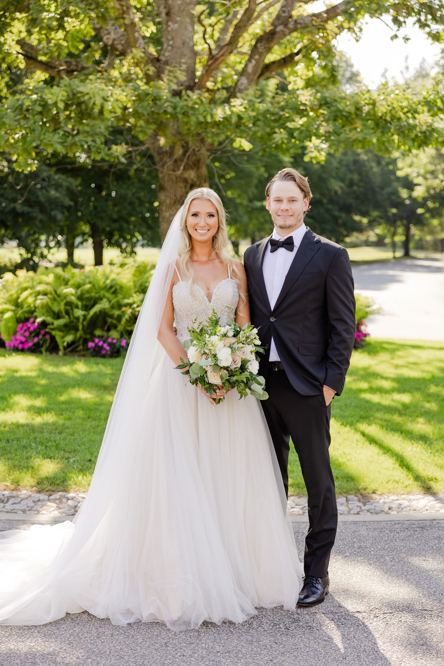 Elegant wedding portrait of a couple standing on a garden path with beautiful green foliage.