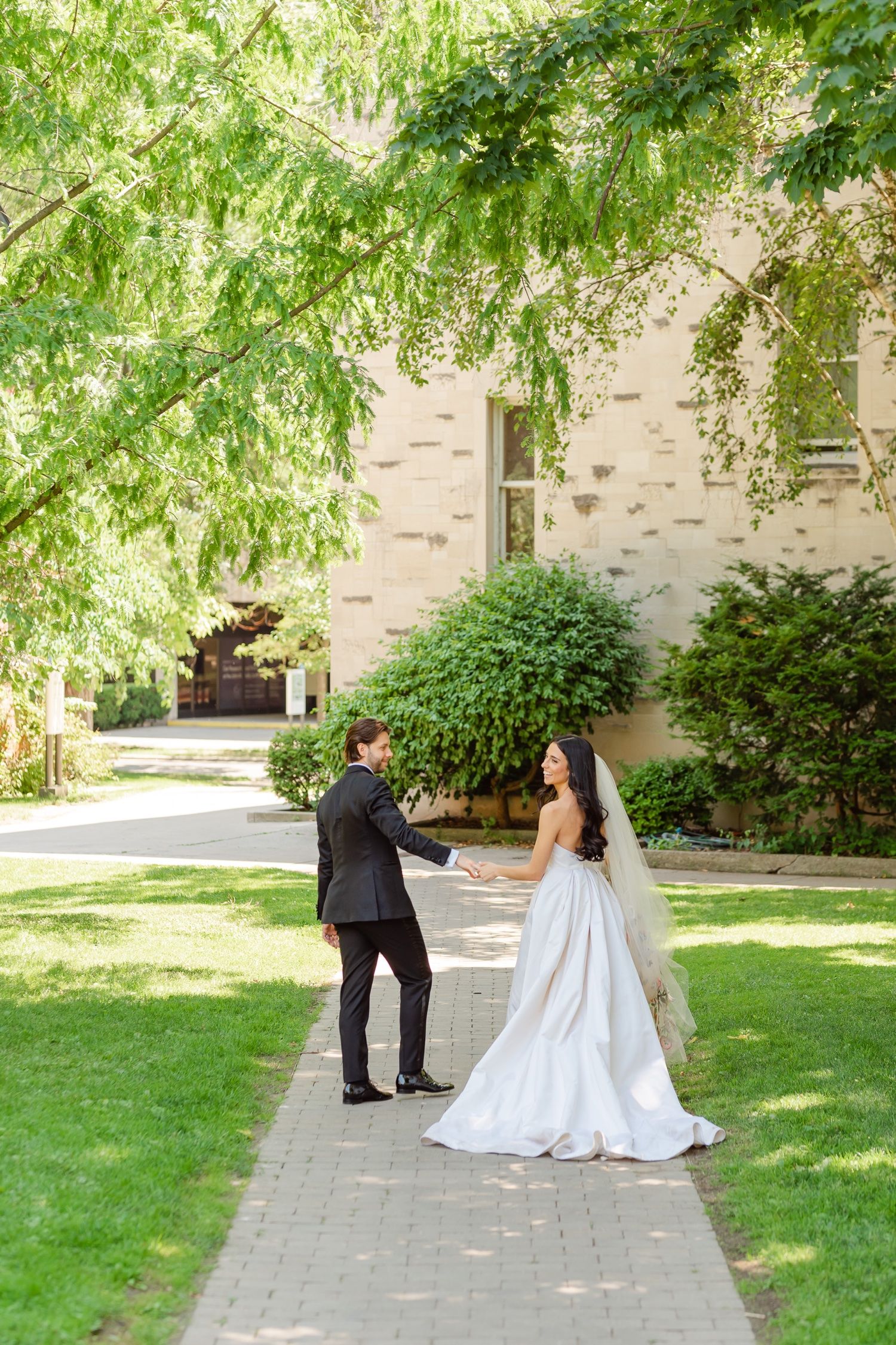 A couple shares a playful moment on a tree-lined pathway during their wedding.
