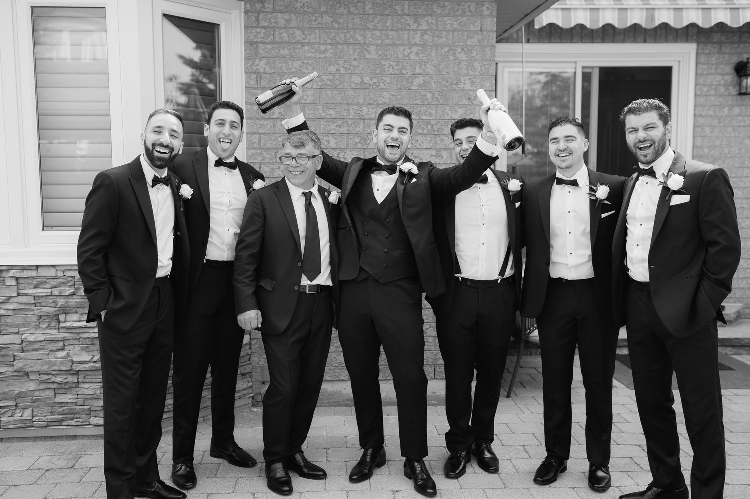 Classic black and white photo of groomsmen in tuxedos posing together outdoors.