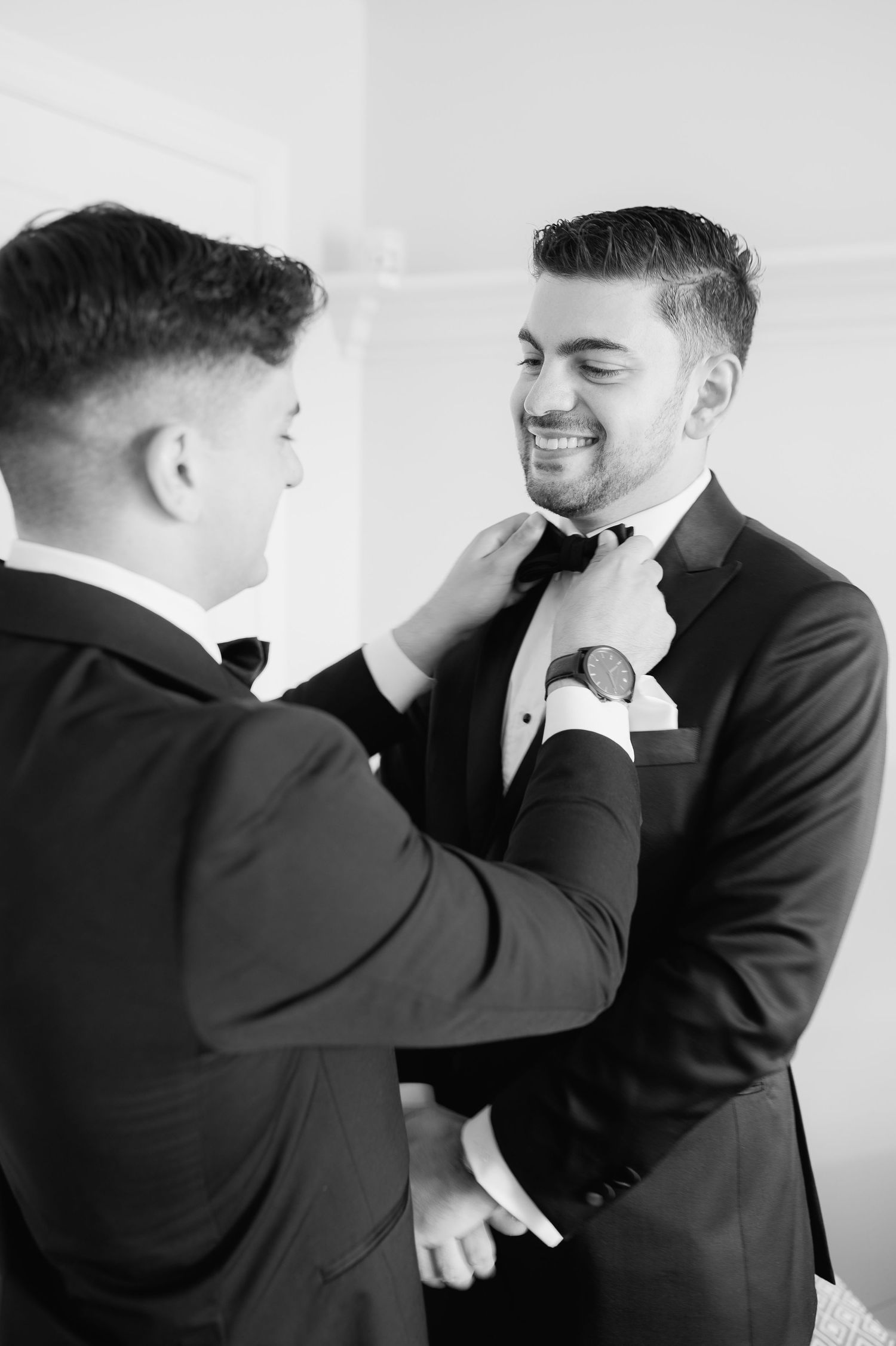 Two people in formal wear help adjust a bowtie in a black and white photo.