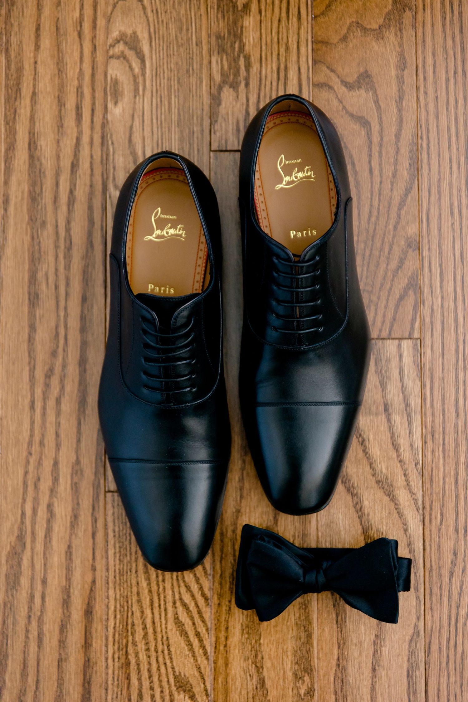 Classic black leather Oxford shoes with black bow tie on hardwood flooring.