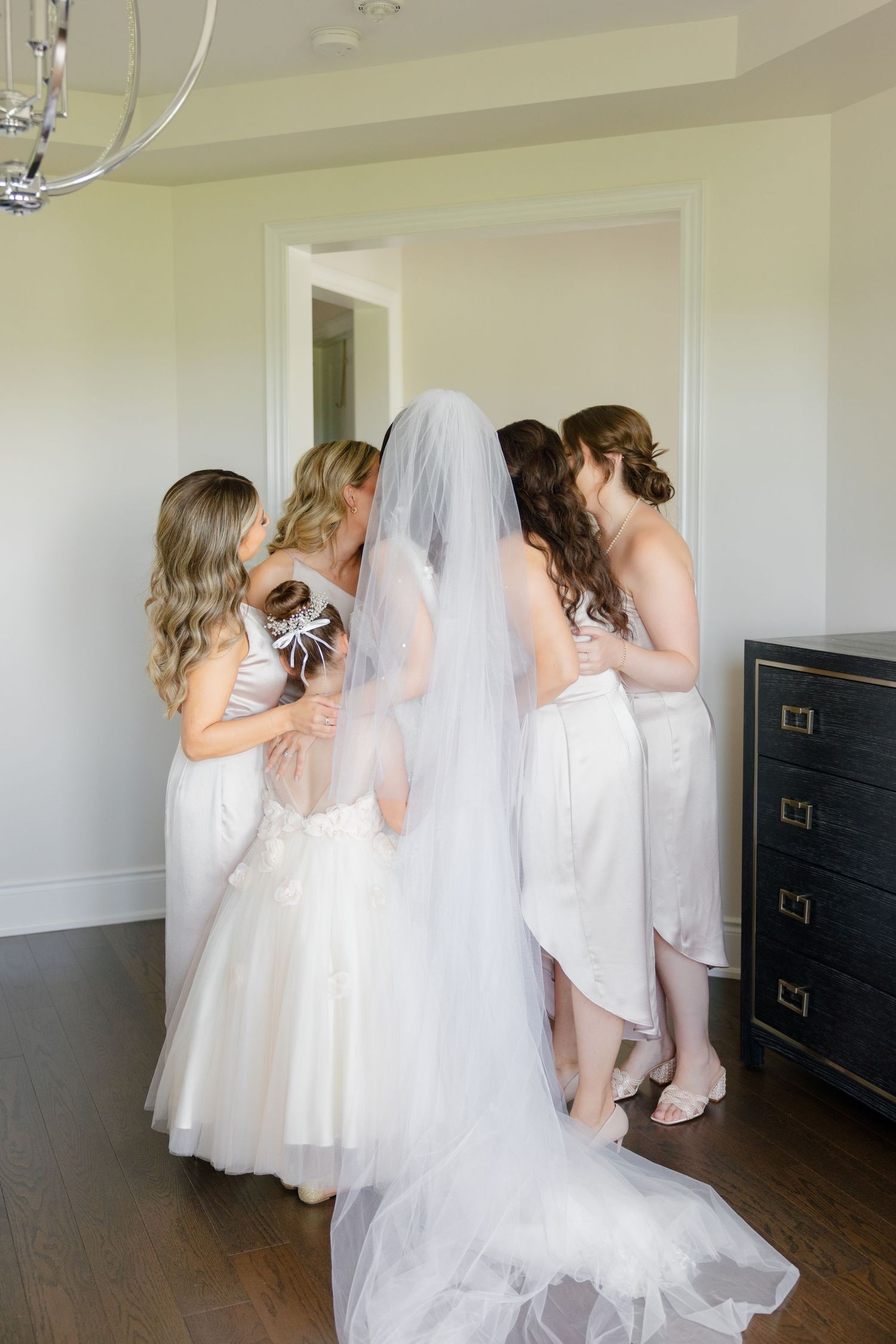 Bridesmaids in light-colored dresses helping with wedding preparations in an elegant room.
