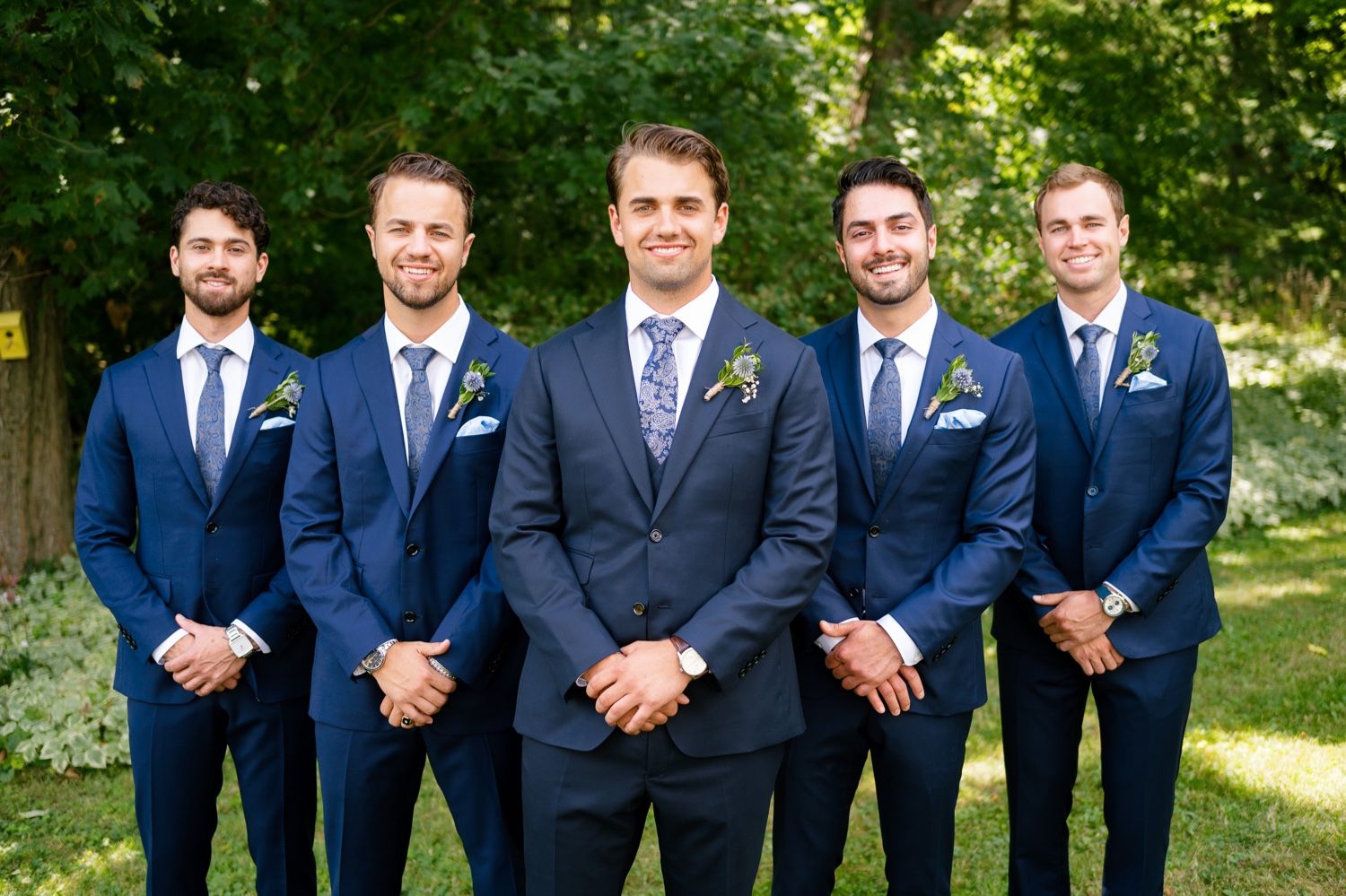 Wedding party in matching navy suits with different colored ties standing in formal pose outdoors.