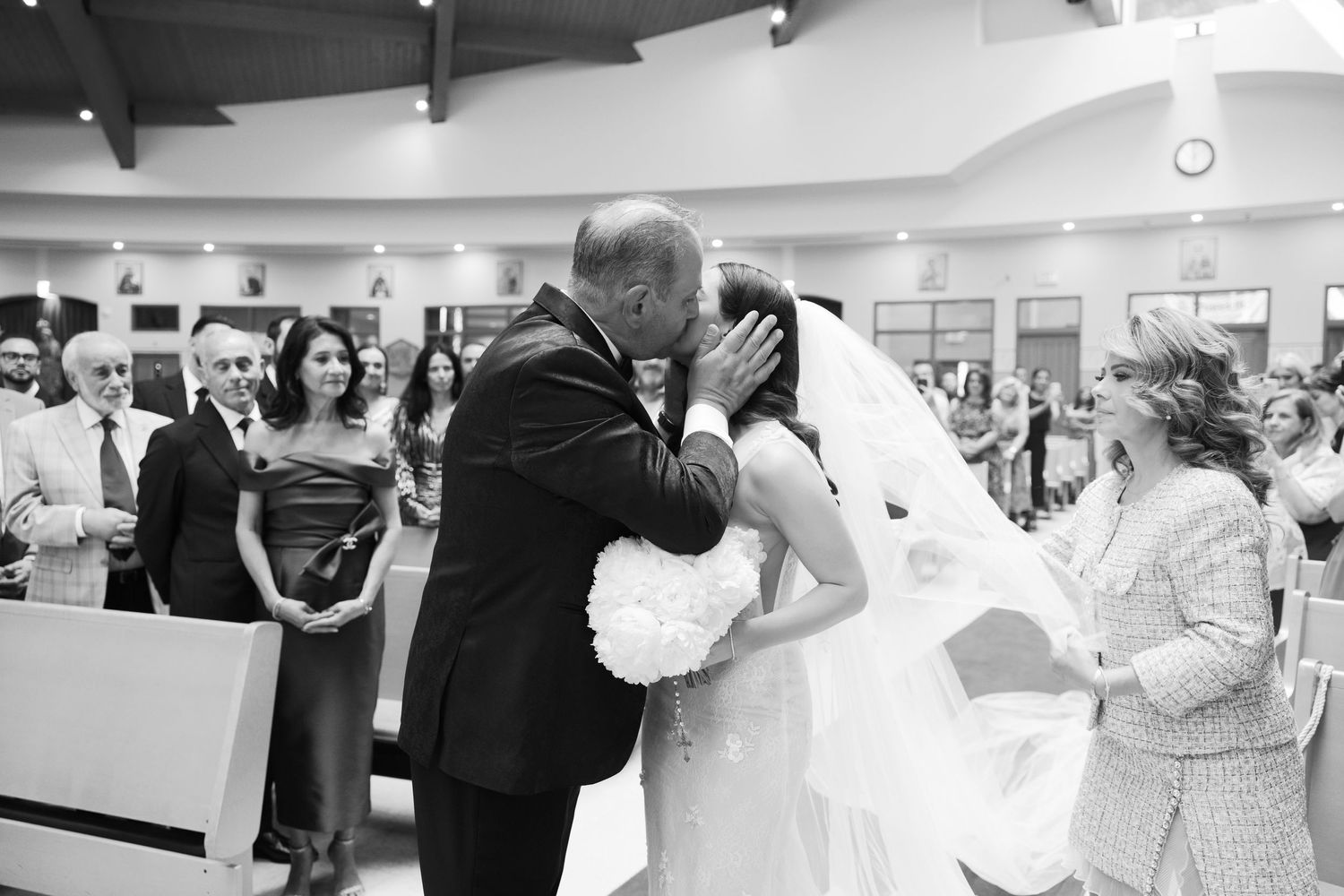Black and white capture of an emotional veil lifting moment during a church wedding ceremony.