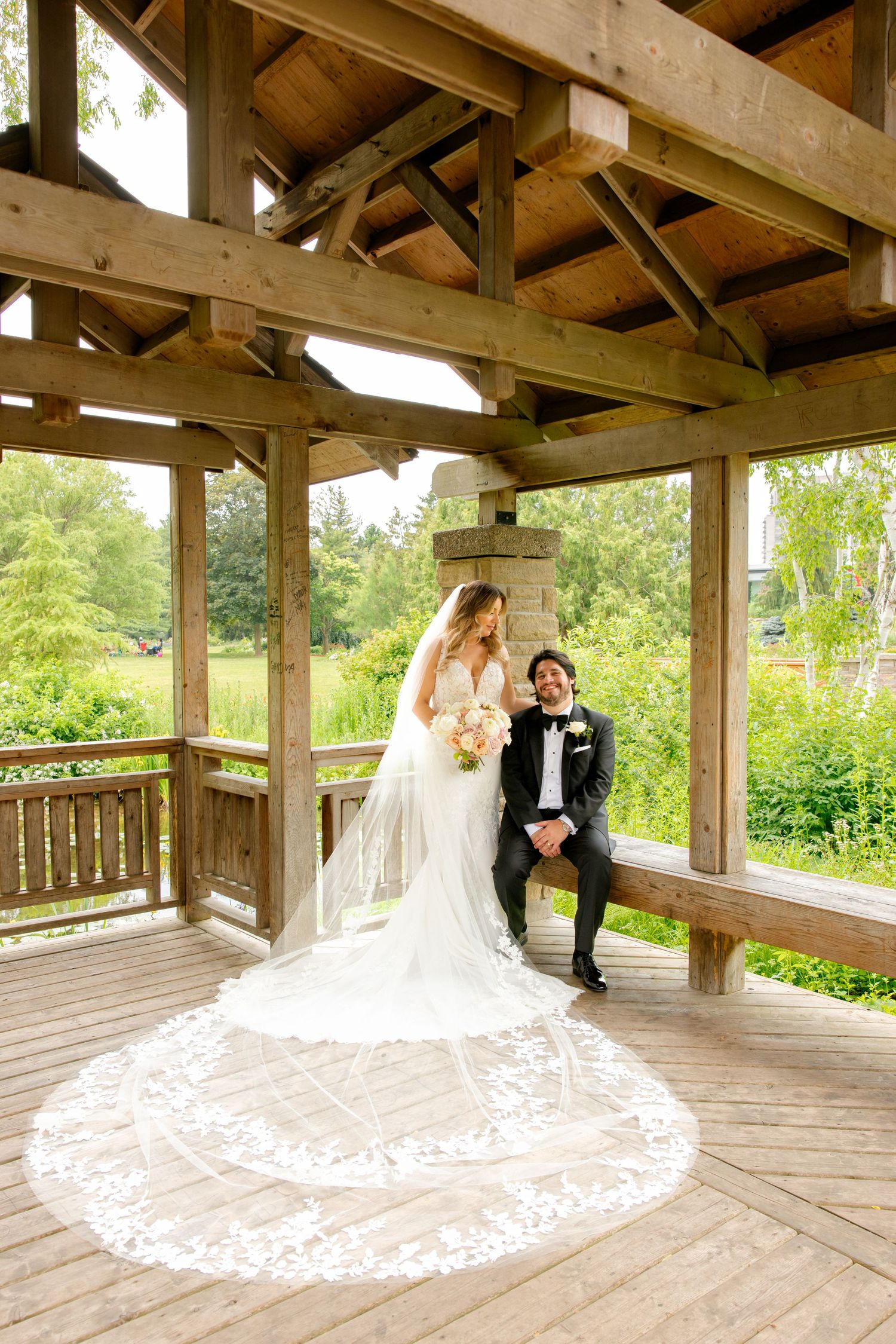 Newlyweds share a moment in garden gazebo with intricate lace veil details.