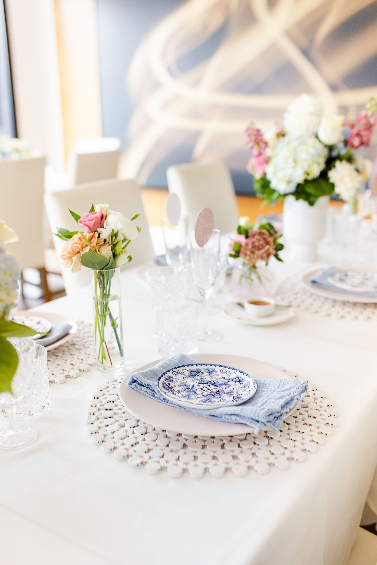 Detailed table setting with blue and white china plate on lace doily and fresh flower centerpiece.