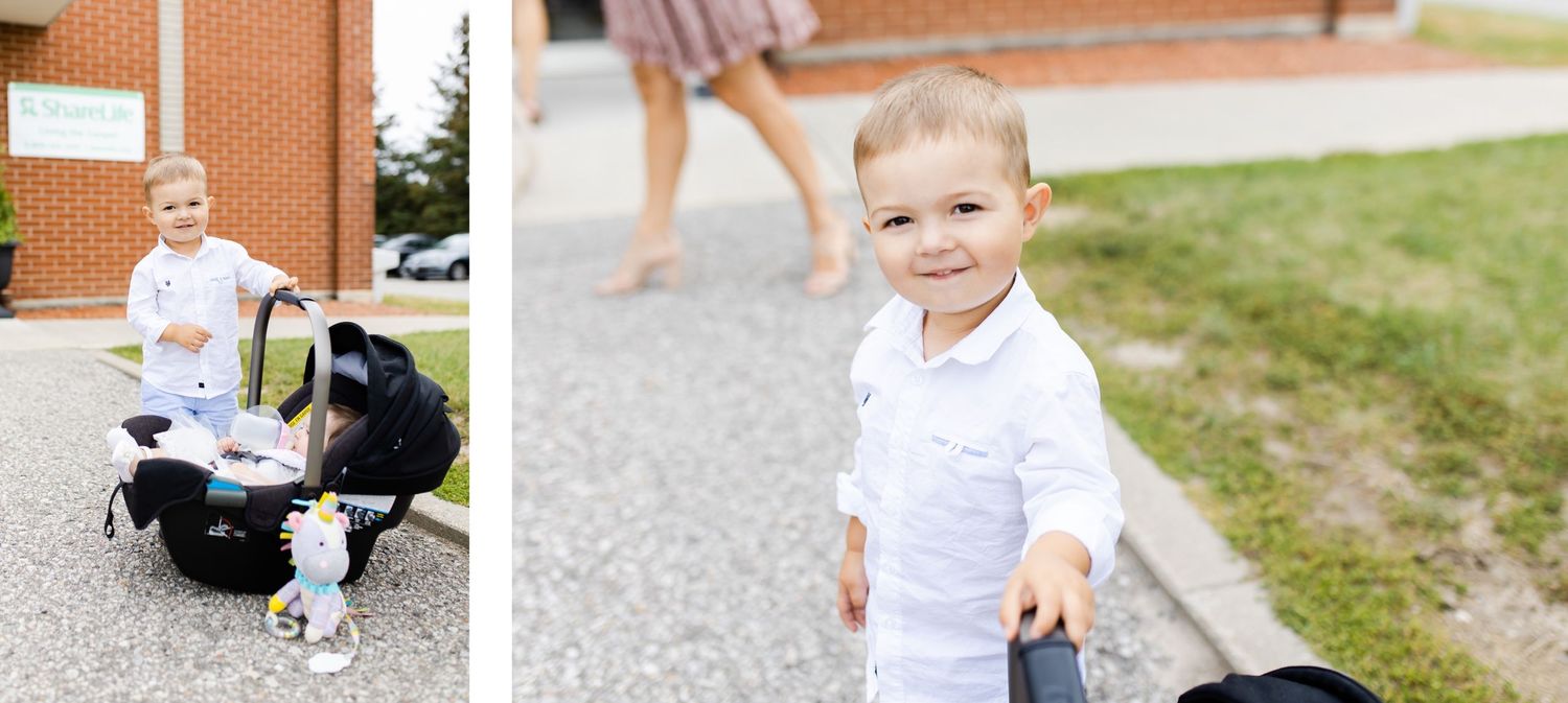 A small child in white clothing walks on a path while a stroller sits in the background.