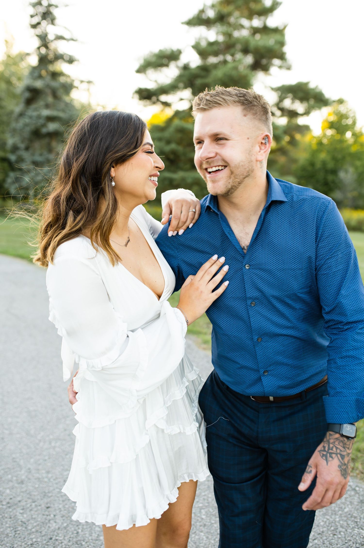 Joyful couple shares a candid moment on path with pine trees in background.