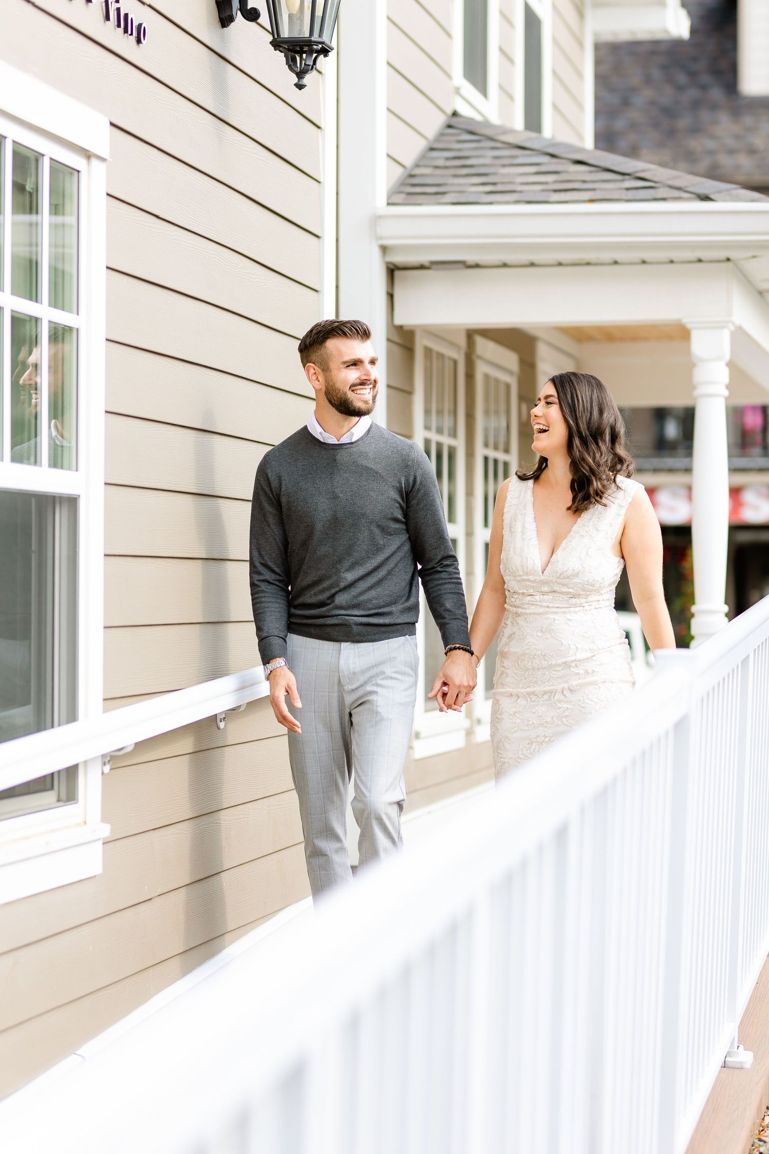 Two people walking along a white railed porch of a beige building.