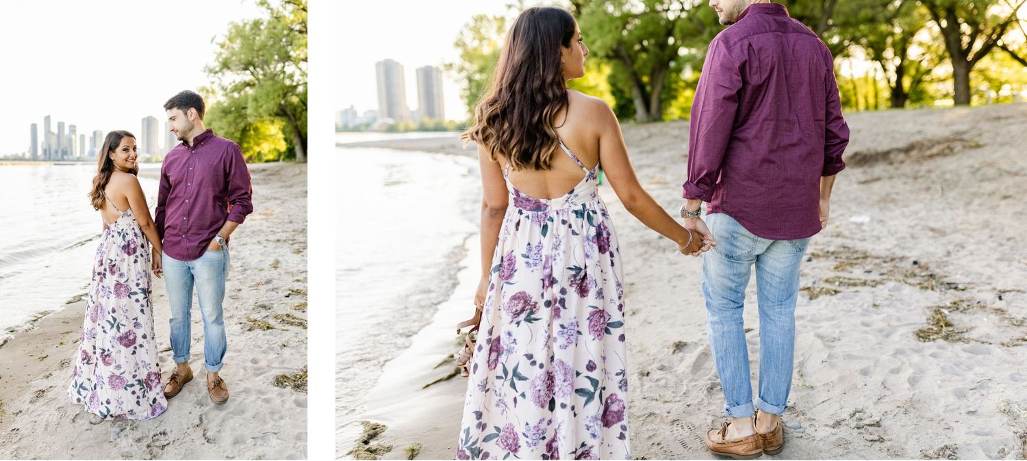 Couple walking together on beach path with city buildings in background.