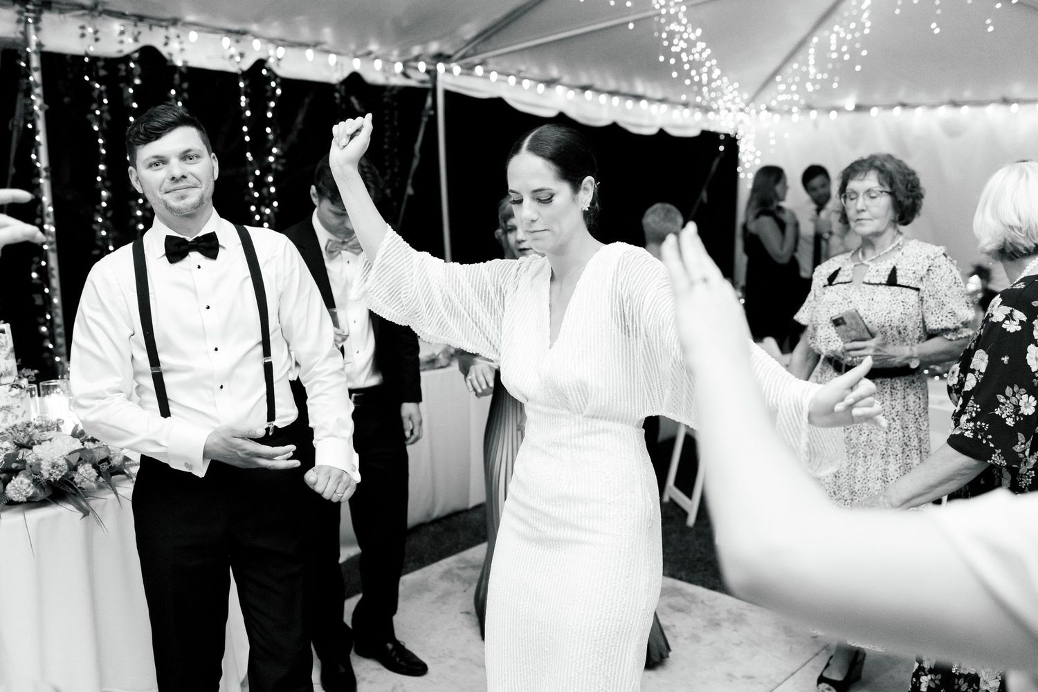 Joyful celebration moment under tent with string lights at wedding reception.