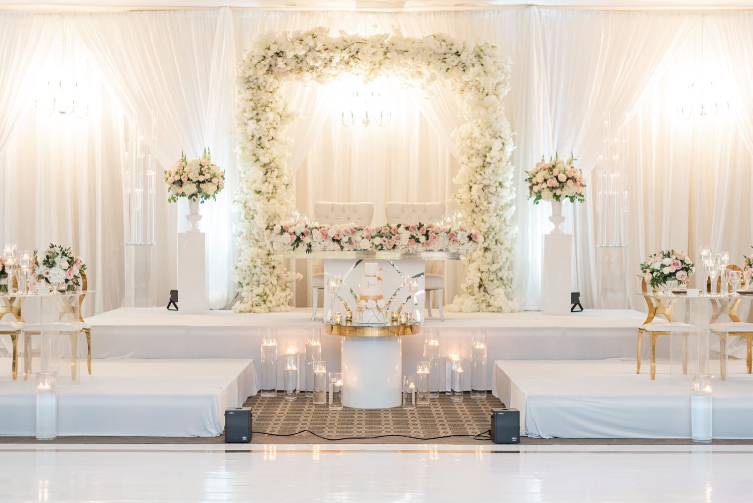 White and floral wedding stage setup with elegant drapery and romantic lighting in a modern venue.