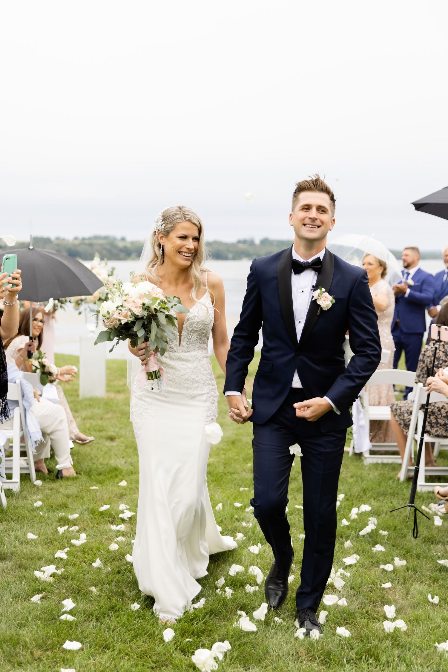Stylish couple walks hand in hand during recessional with flower petals falling.
