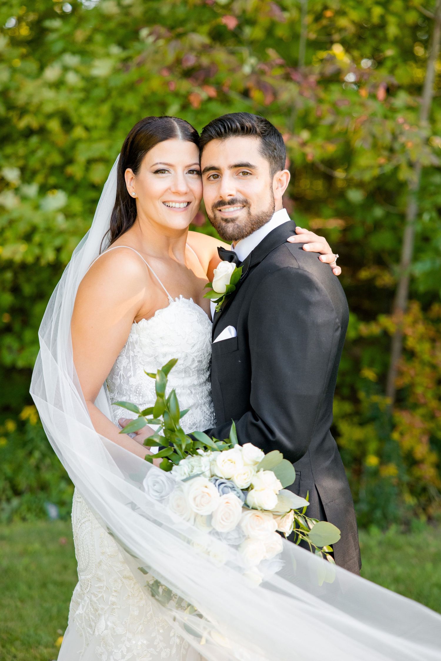 Joyful wedding portrait outdoors with couple holding beautiful white and green bouquet.