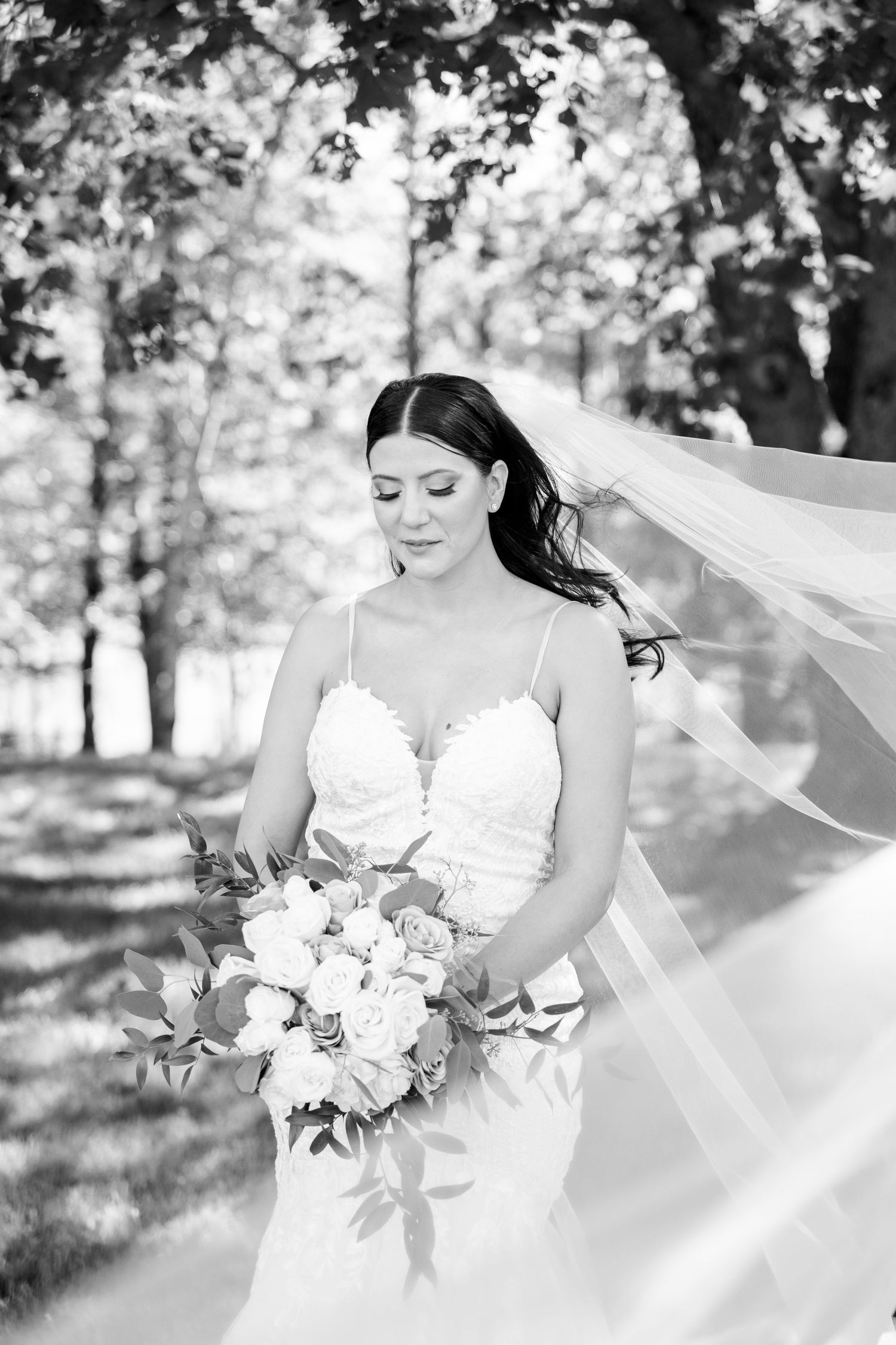 Black and white portrait of bride with flowing veil in garden setting.
