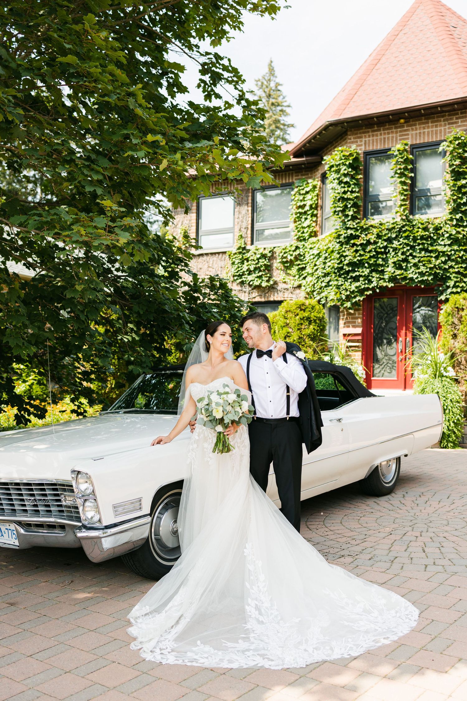 Elegant wedding scene with a vintage white Cadillac parked in front of an ivy-covered brick building.