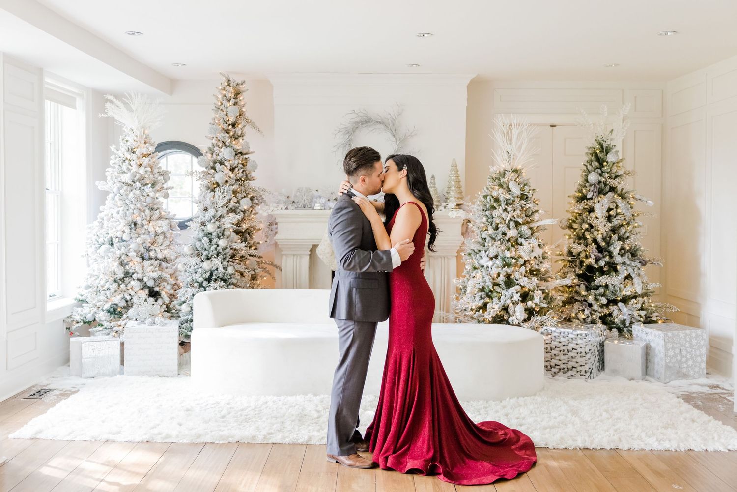A romantic moment captured in front of snow-flocked Christmas trees and white holiday decor.