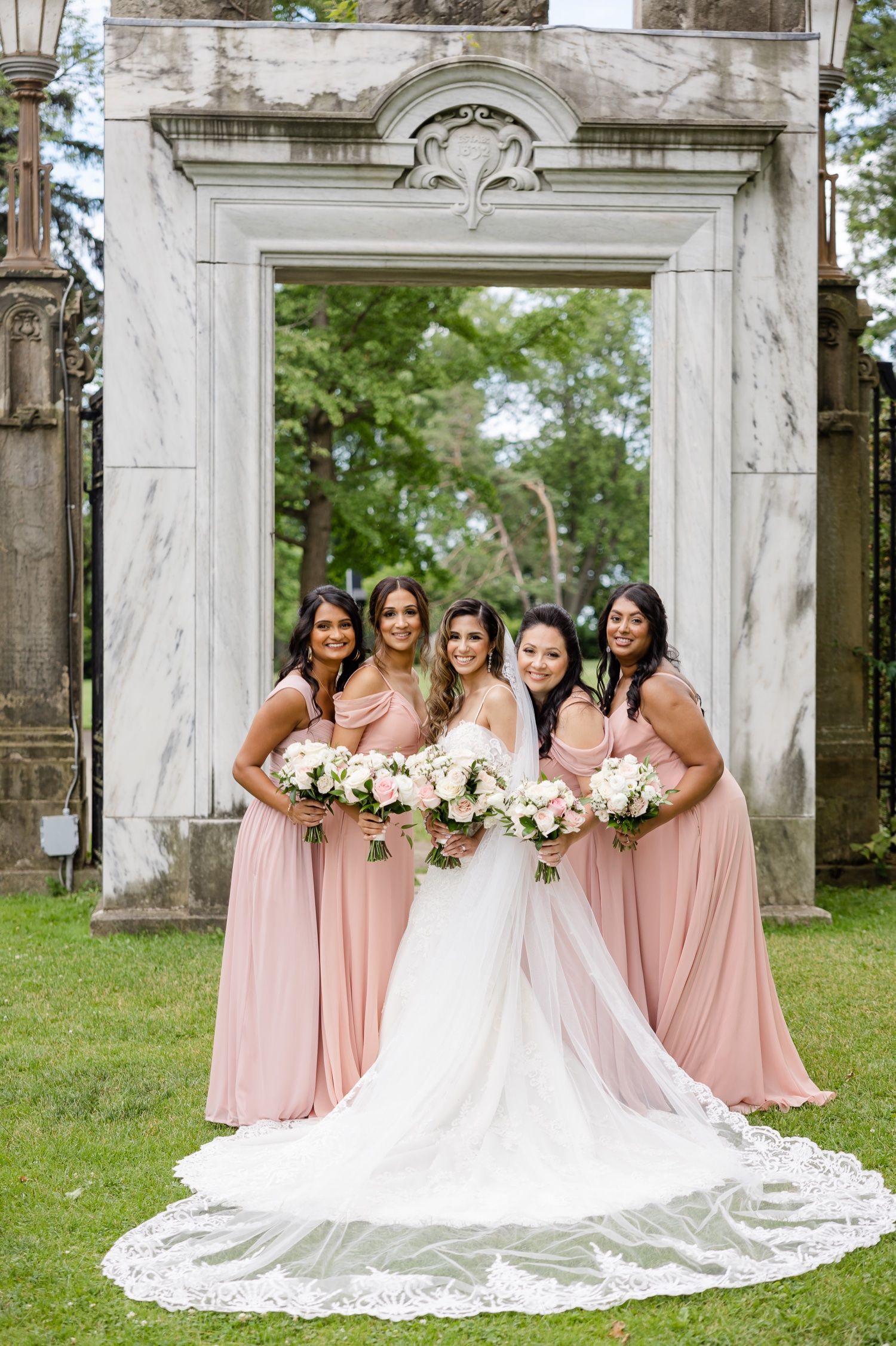 Wedding party poses under marble archway with bridesmaids in flowing pink gowns.