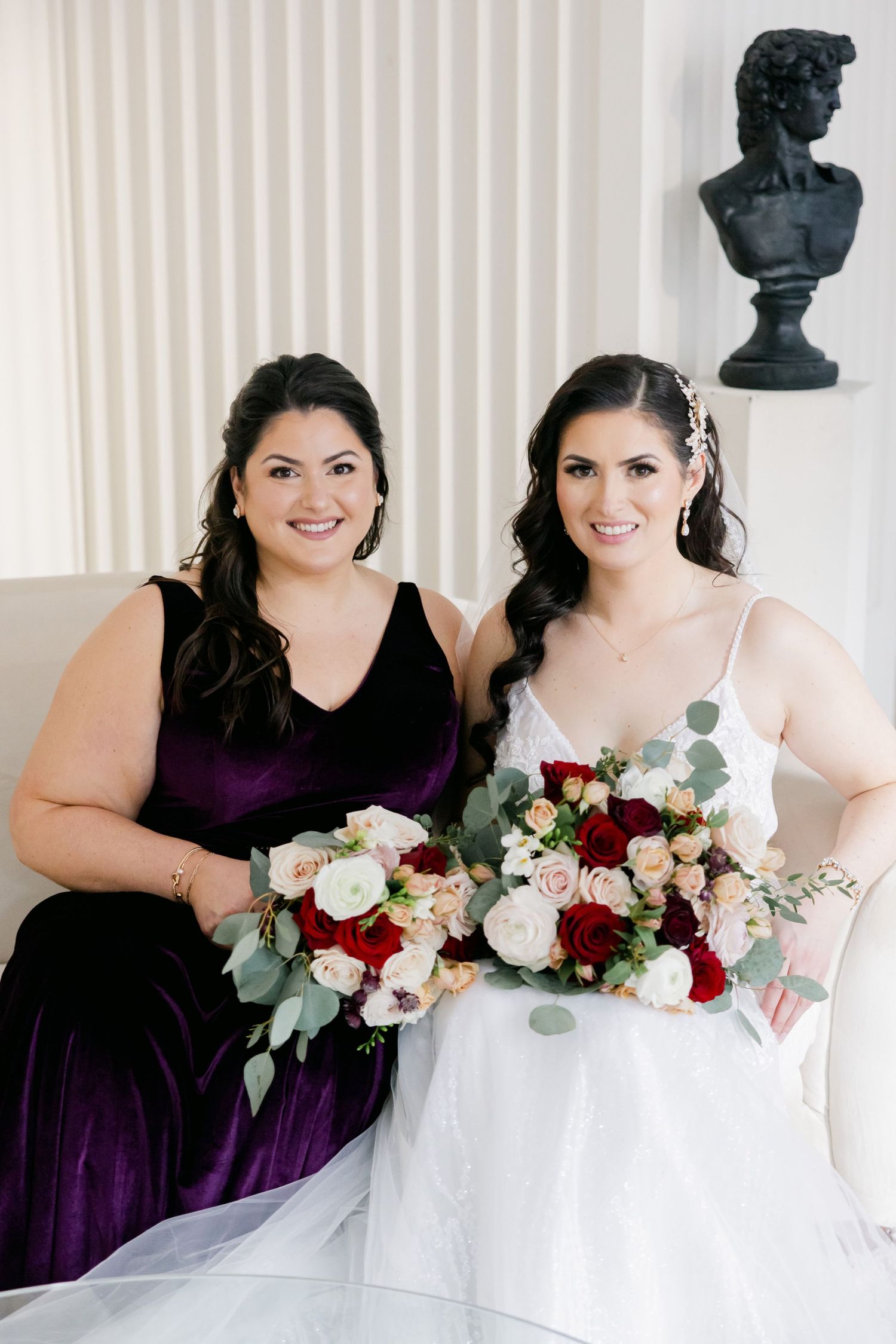 Two wedding party members pose together holding elegant burgundy and white floral bouquets.