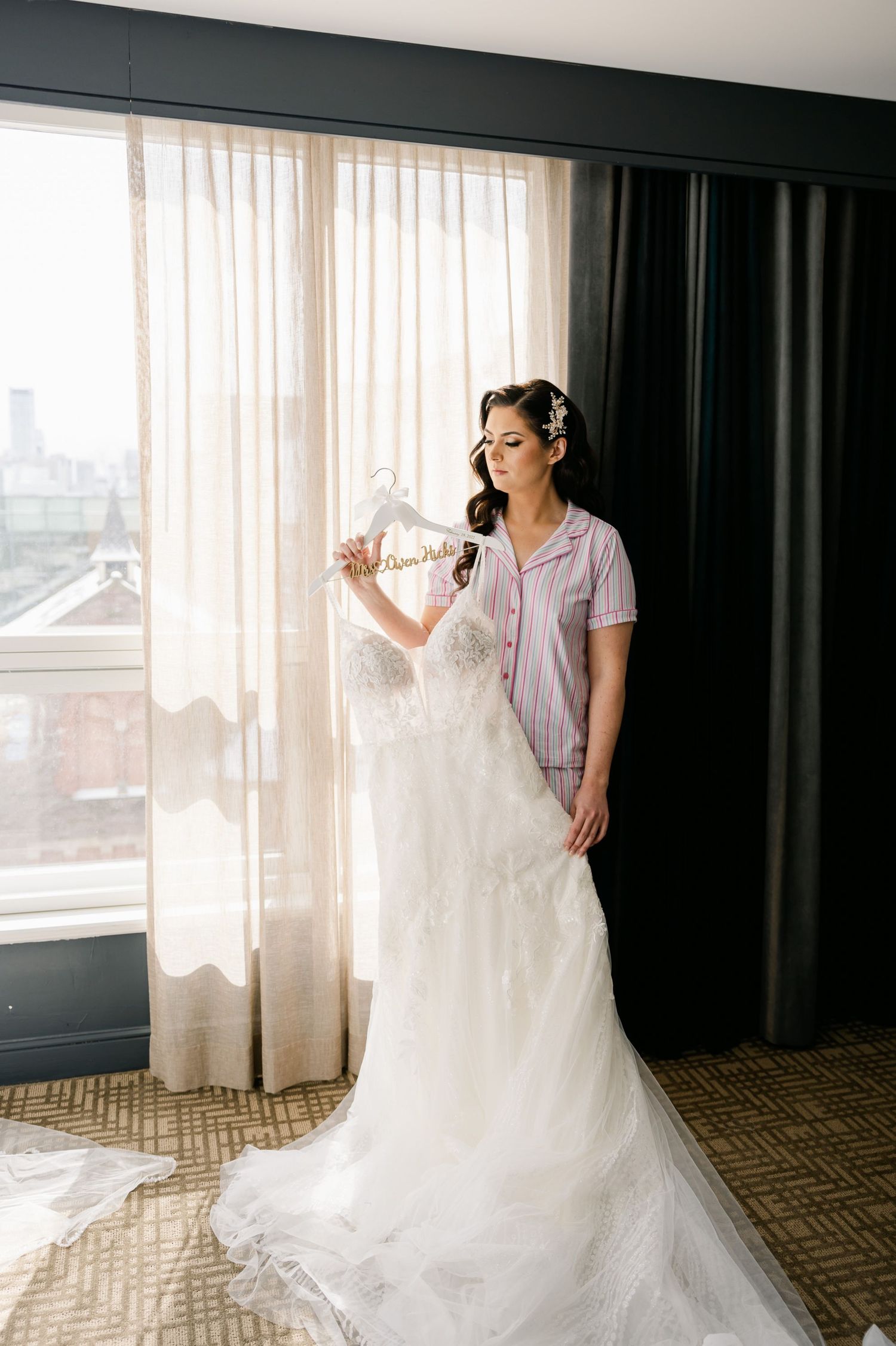Wedding dress hanging by window while being prepared for bridal wear.