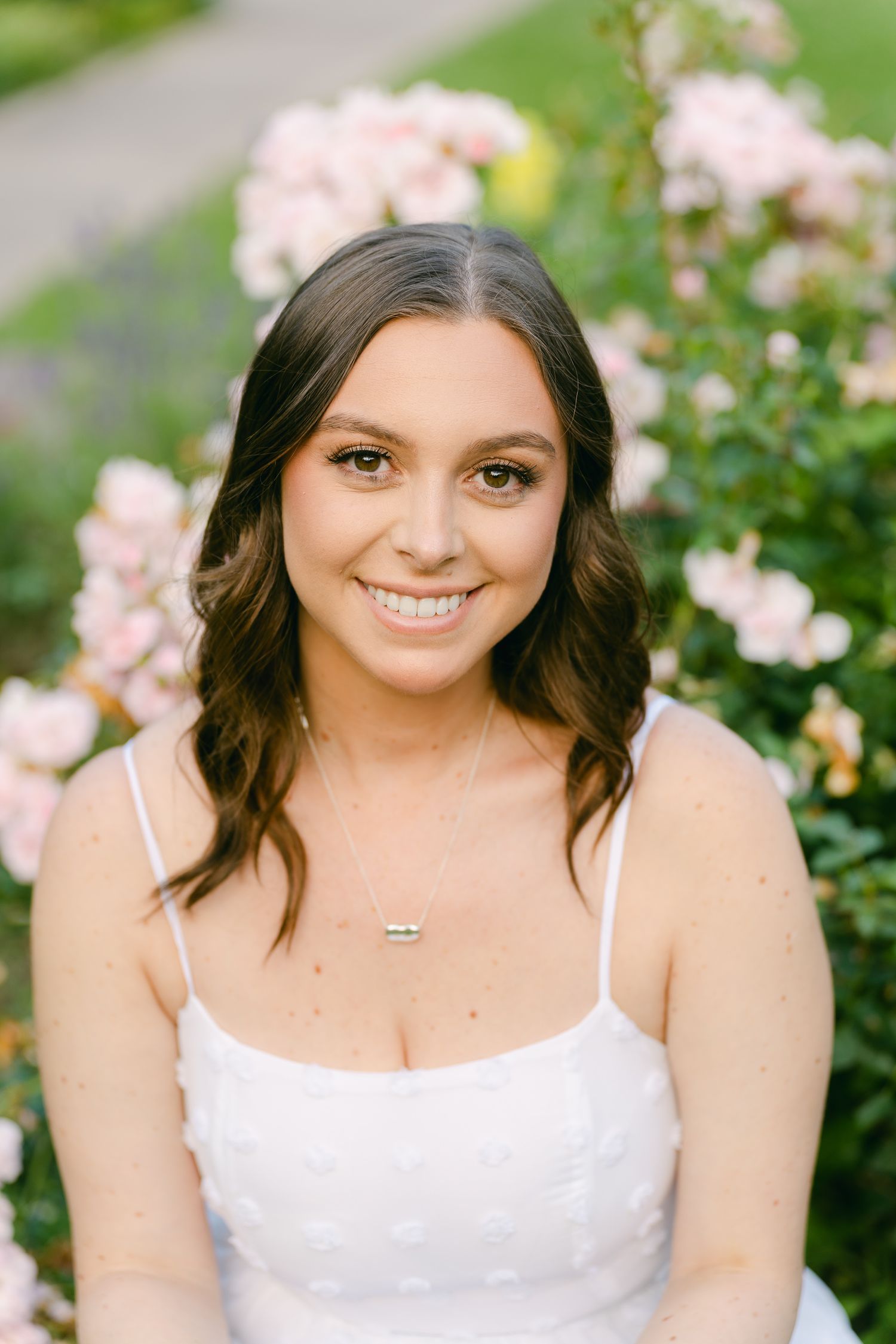 Portrait of a woman in white dress smiling against pink floral garden background.