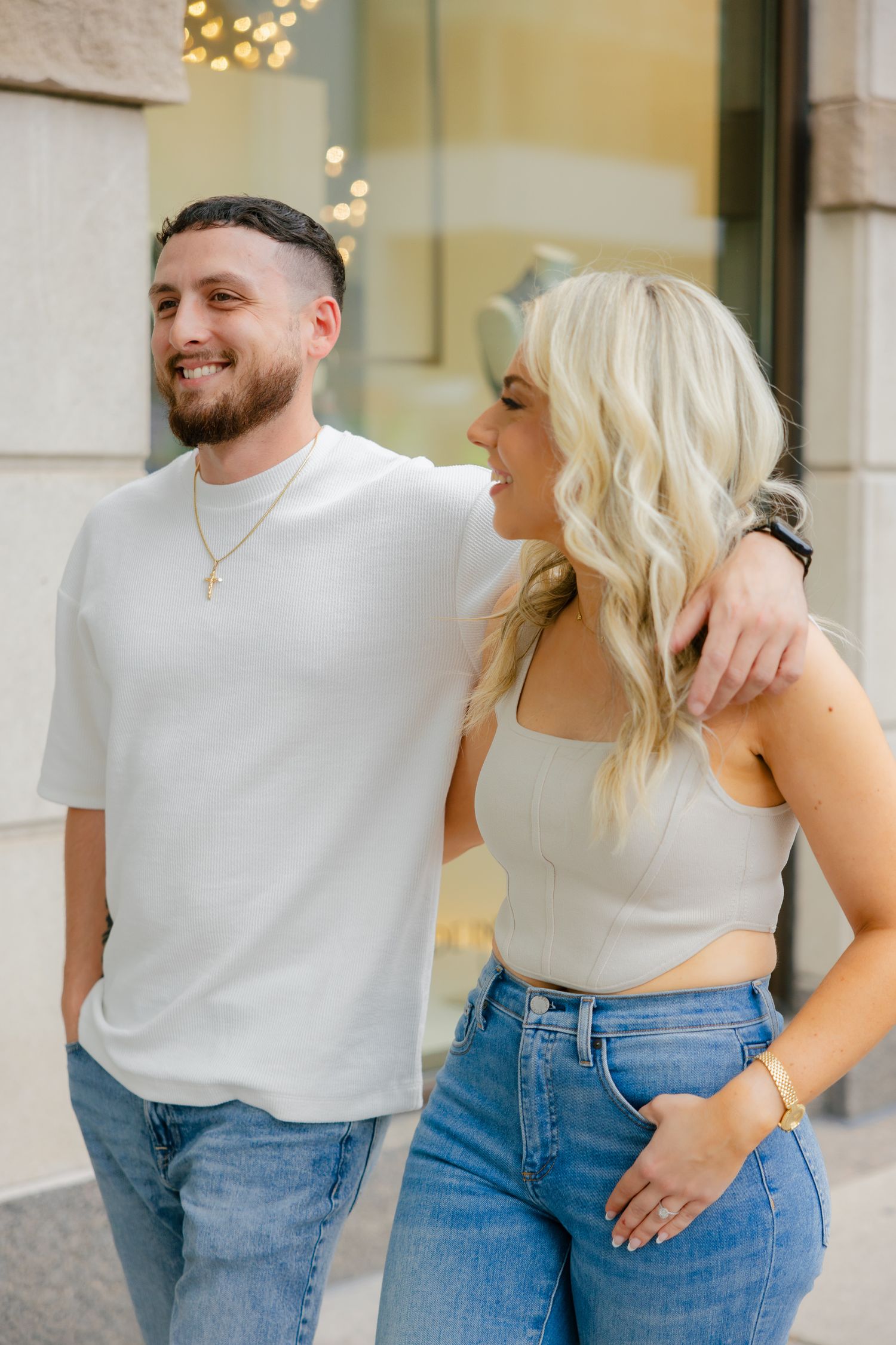 Casual couple in coordinated white and denim outfits embrace while smiling outdoors.