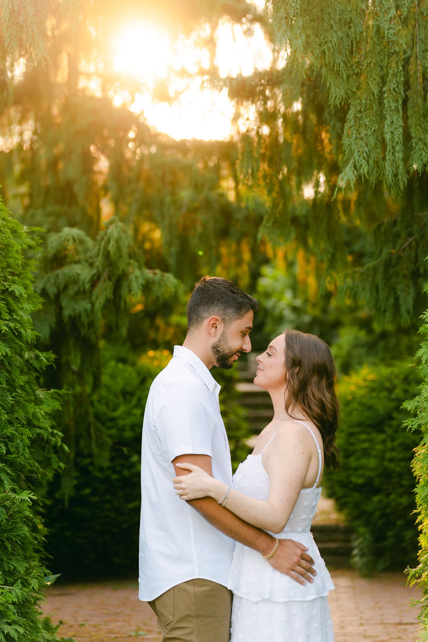 Romantic sunset portrait of a couple embracing on a garden path with glowing backlight.