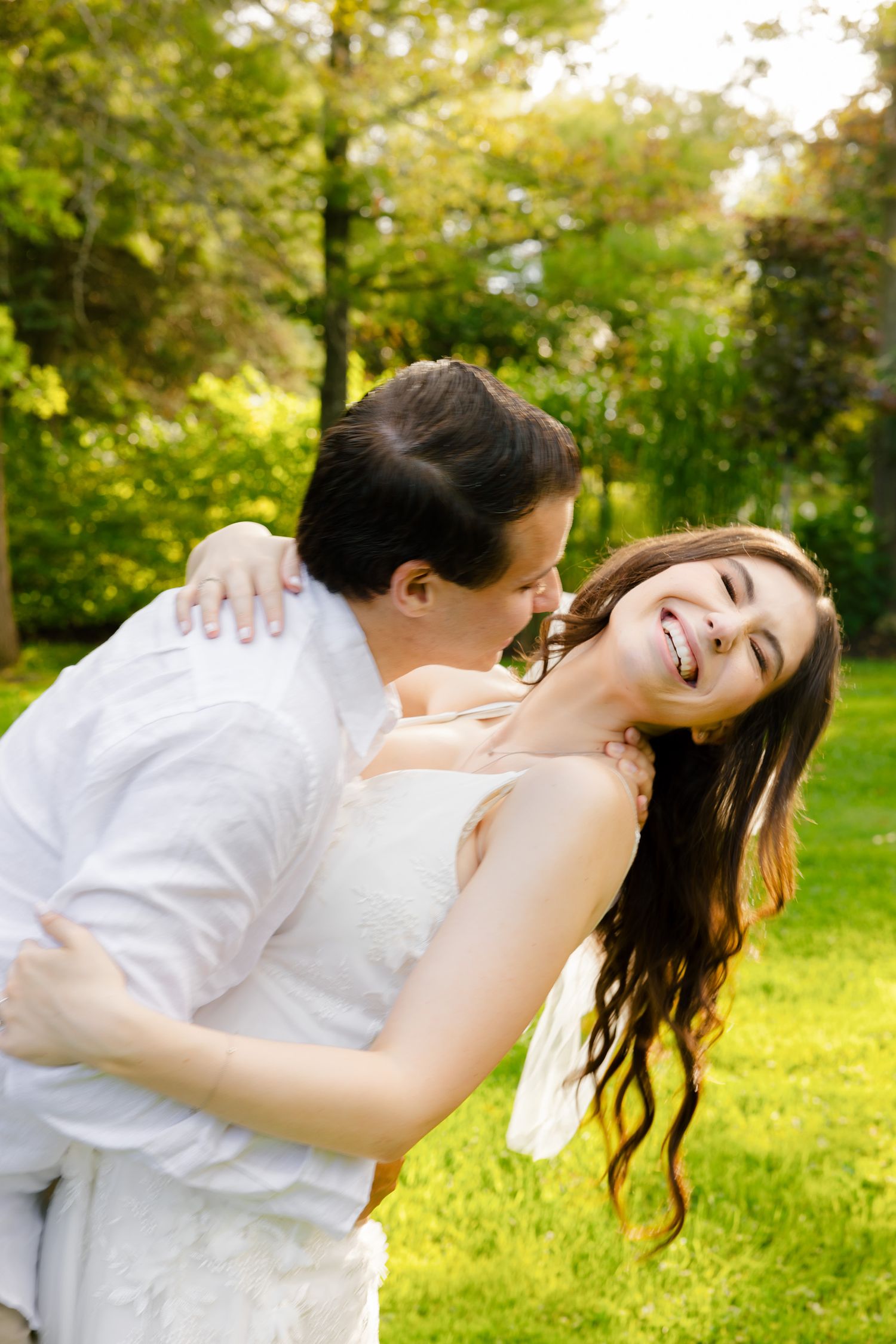 A joyful couple sharing a playful moment in a sunlit garden setting.
